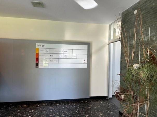 Heller Eingangsbereich mit Informationswand und dekorativen Elementen, dunkler Terrazzoboden.