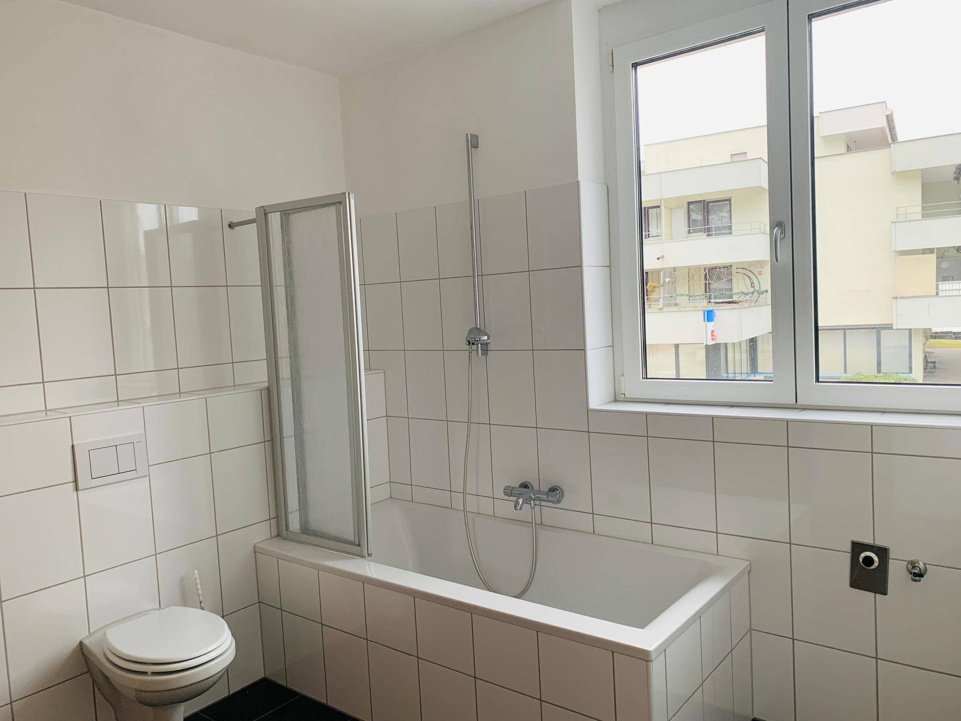Badezimmer mit Badewanne, Duschabtrennung, WC und Fenster für Tageslicht.