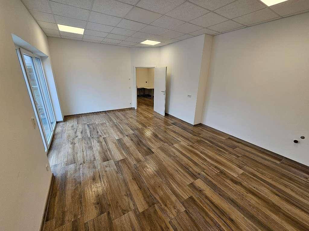 Großer, heller Büroraum mit Holzfliesenboden und großen Fenstern, die viel natürliches Licht hereinlassen.