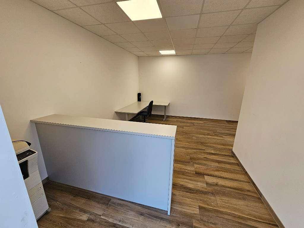 Heller Büroraum mit Empfangstheke und Schreibtisch, ausgestattet mit modernem Holzfliesenboden.