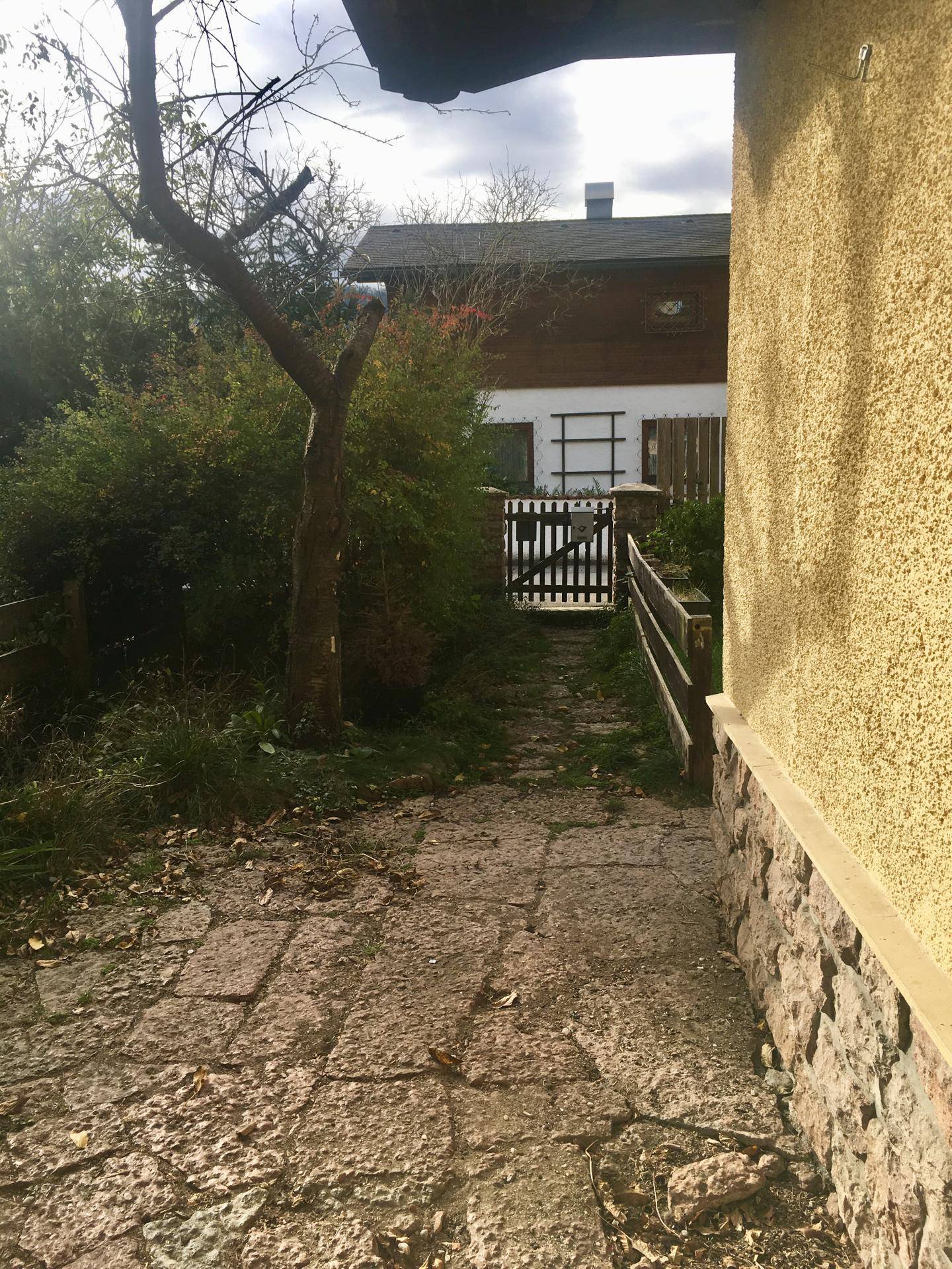 Steinweg führt durch den Garten zu einem Holzzaun und Tor.