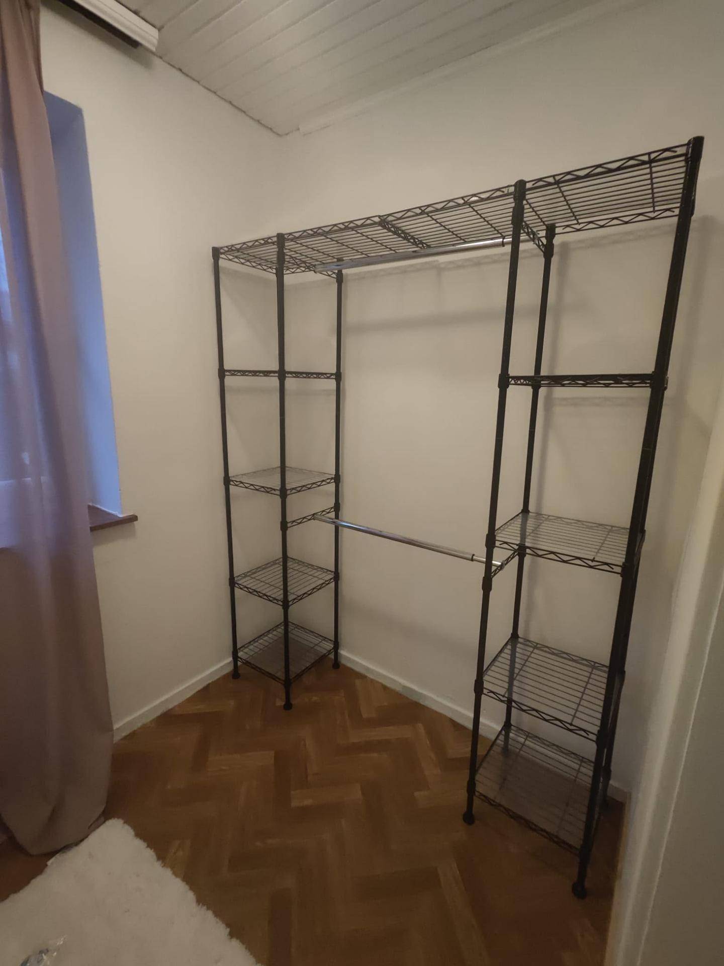 Kleiner Raum mit offenem Metallregalsystem zur Kleideraufbewahrung und Parkettboden.