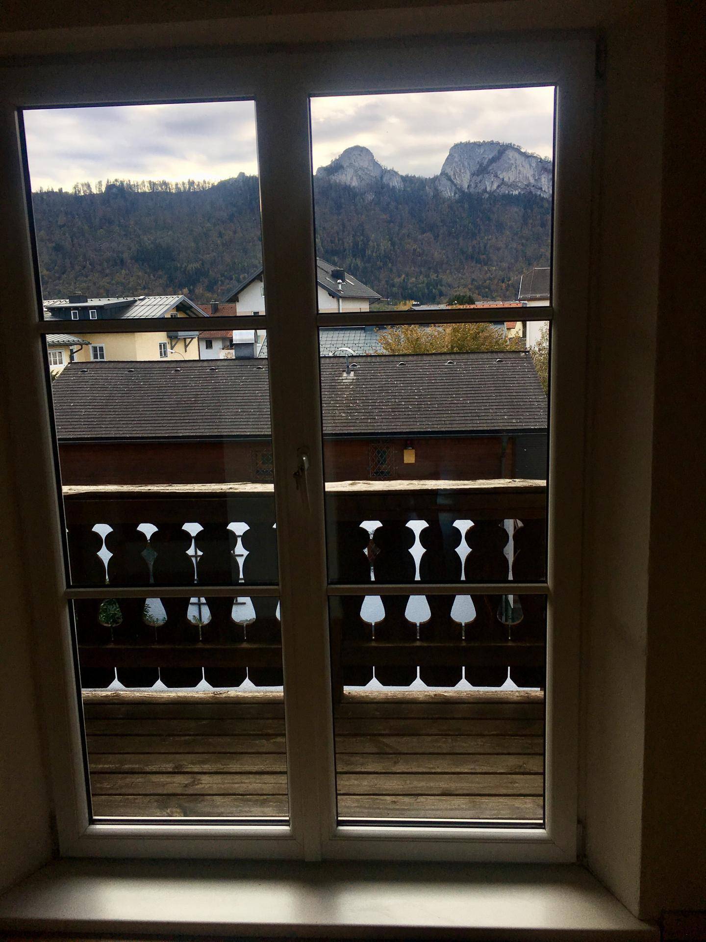 Fensterblick auf eine Berglandschaft und den traditionellen Balkon des Hauses.