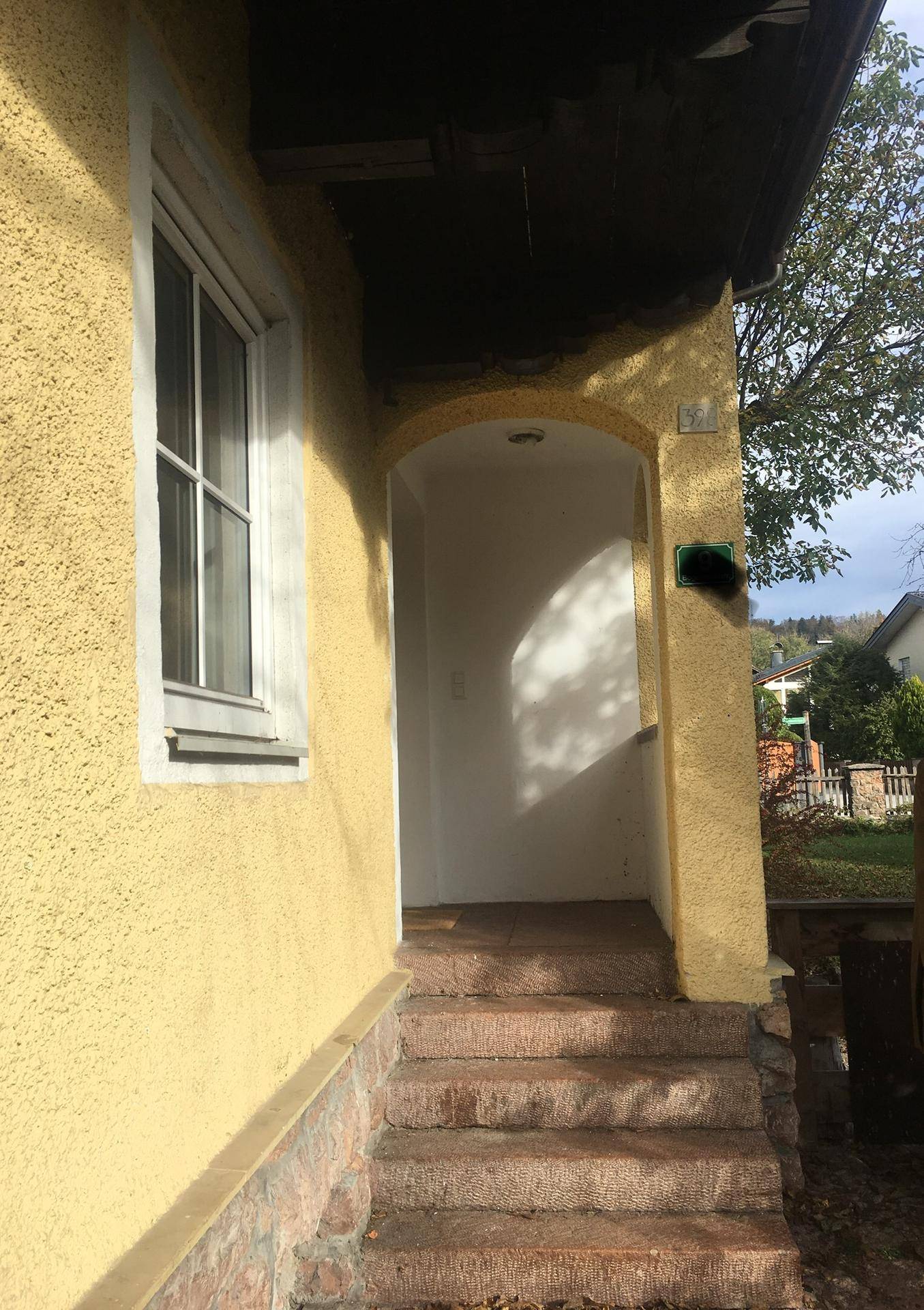 Eingangsbereich des Hauses mit Steinstufen und gelber Putzfassade.
