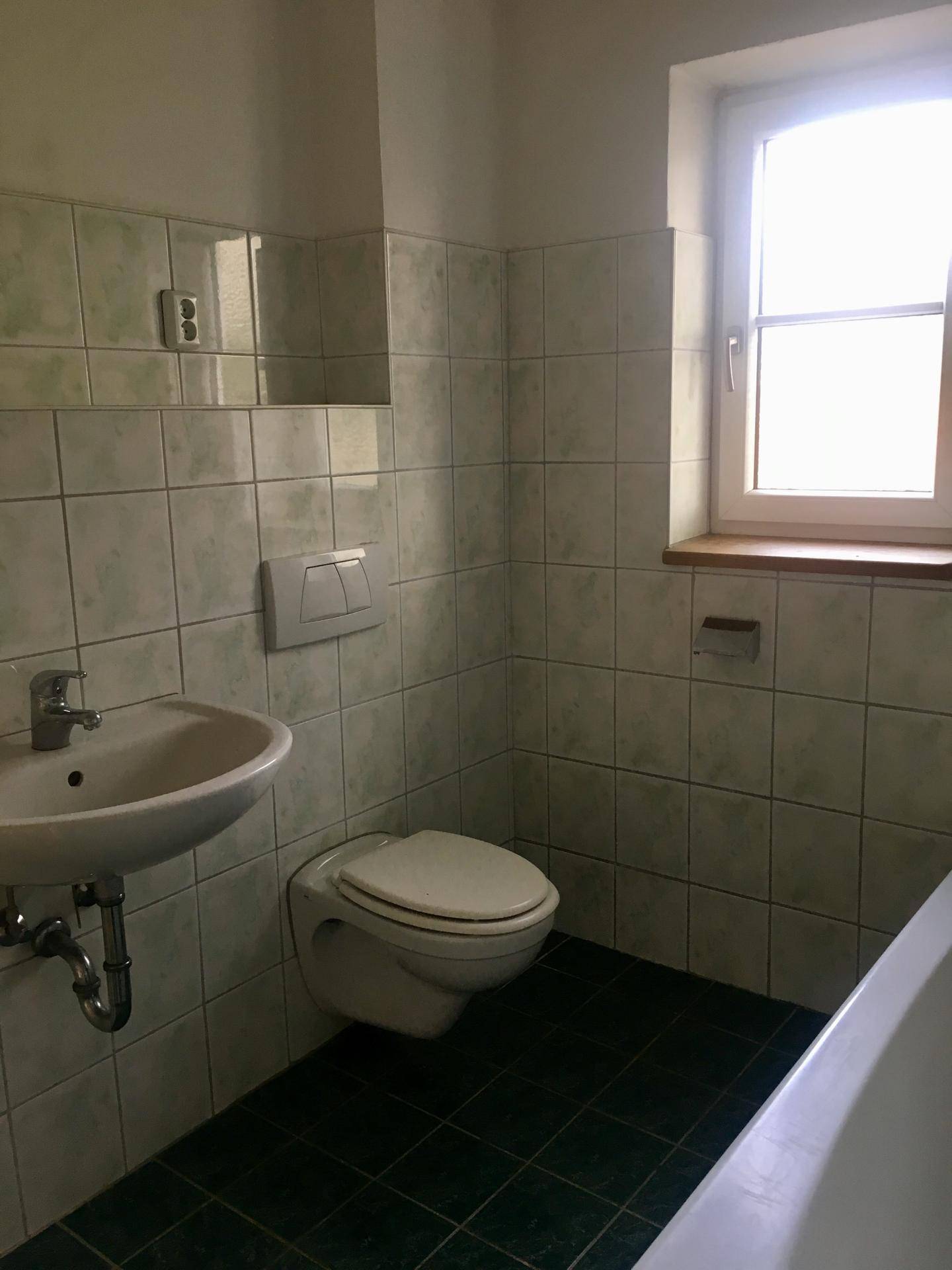 Badezimmer mit hellgrünen Fliesen, Waschbecken, Toilette und Fenster.
