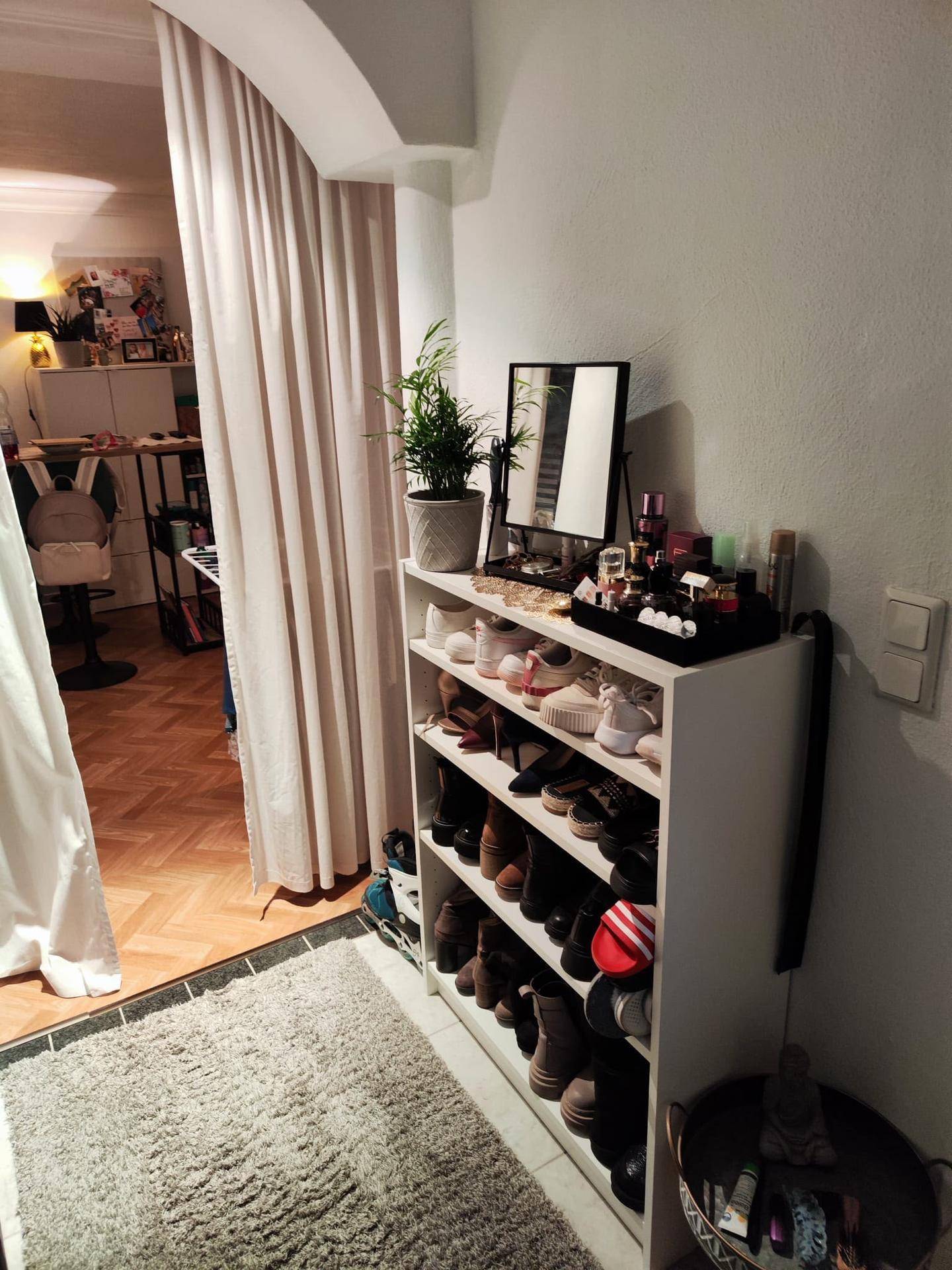 Eingangsbereich mit Schuhregal, Spiegel und einem Vorhang, der zu einem weiteren Raum führt.