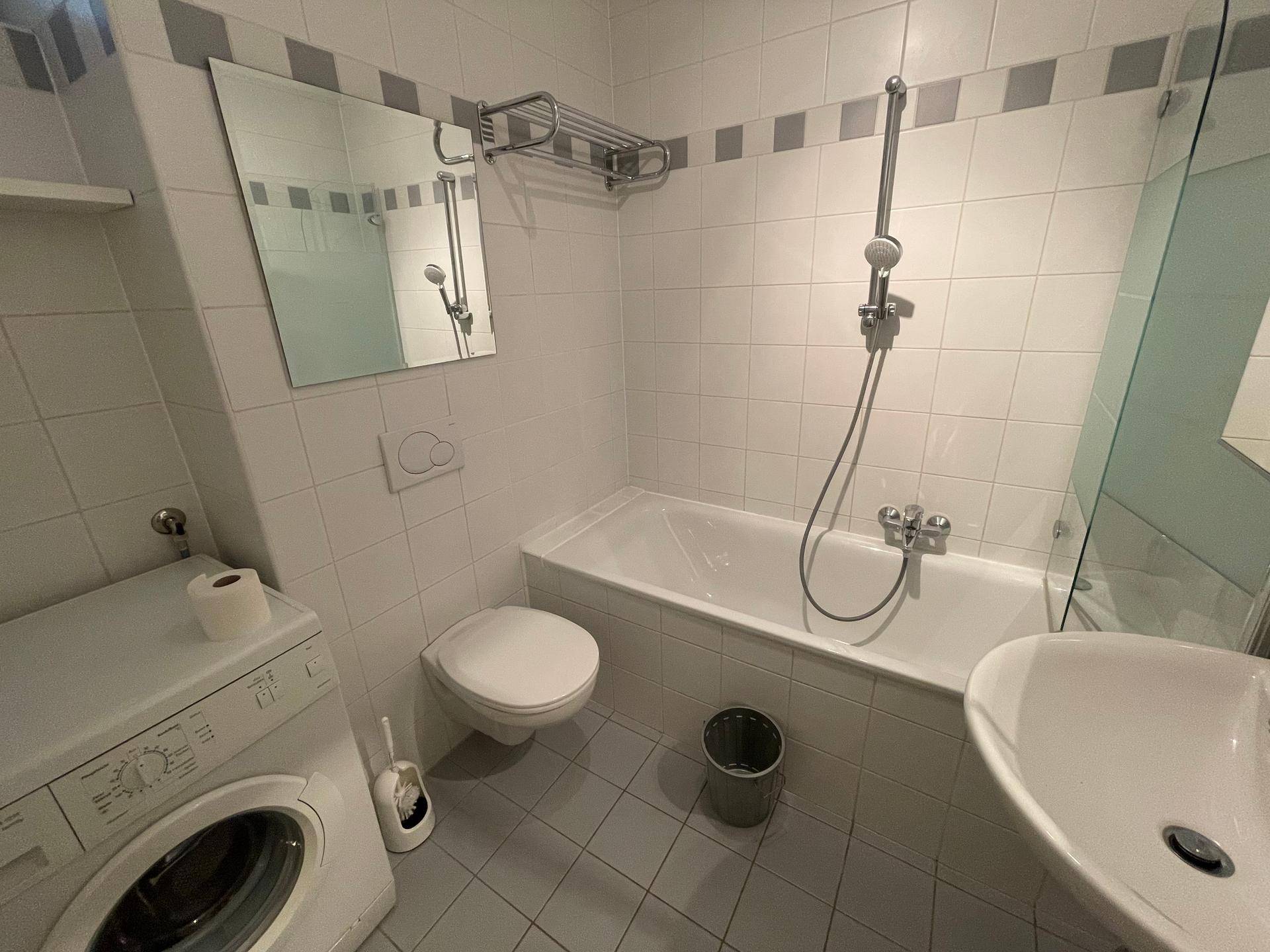 Gefliestes Badezimmer mit Badewanne, Dusche und Waschmaschine.