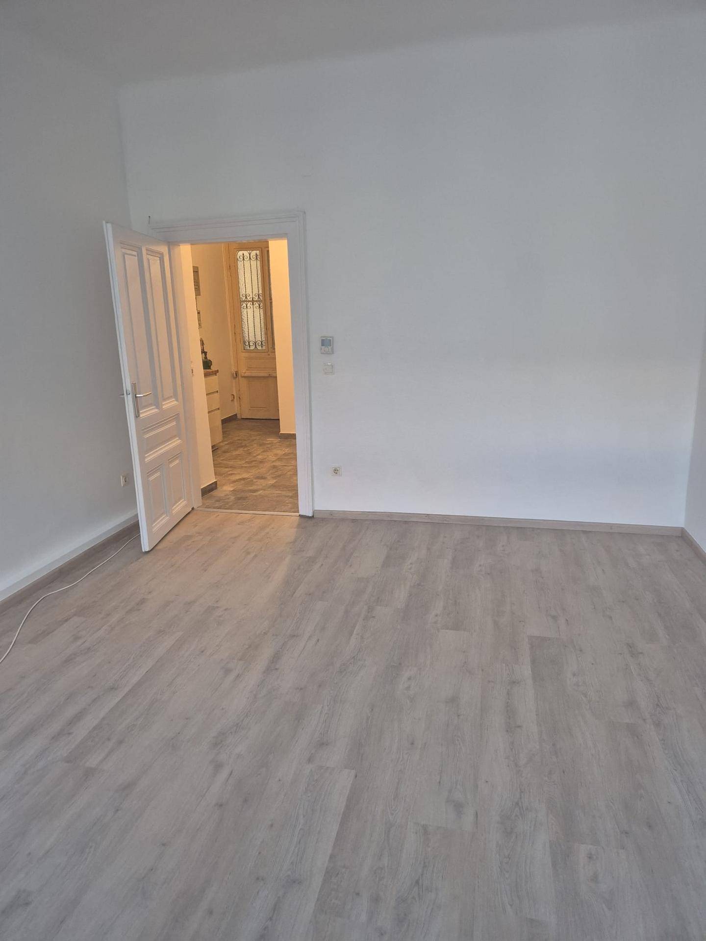 Geräumiges, leeres Zimmer mit hellem Laminatboden und Zugang zu einem weiteren Raum.