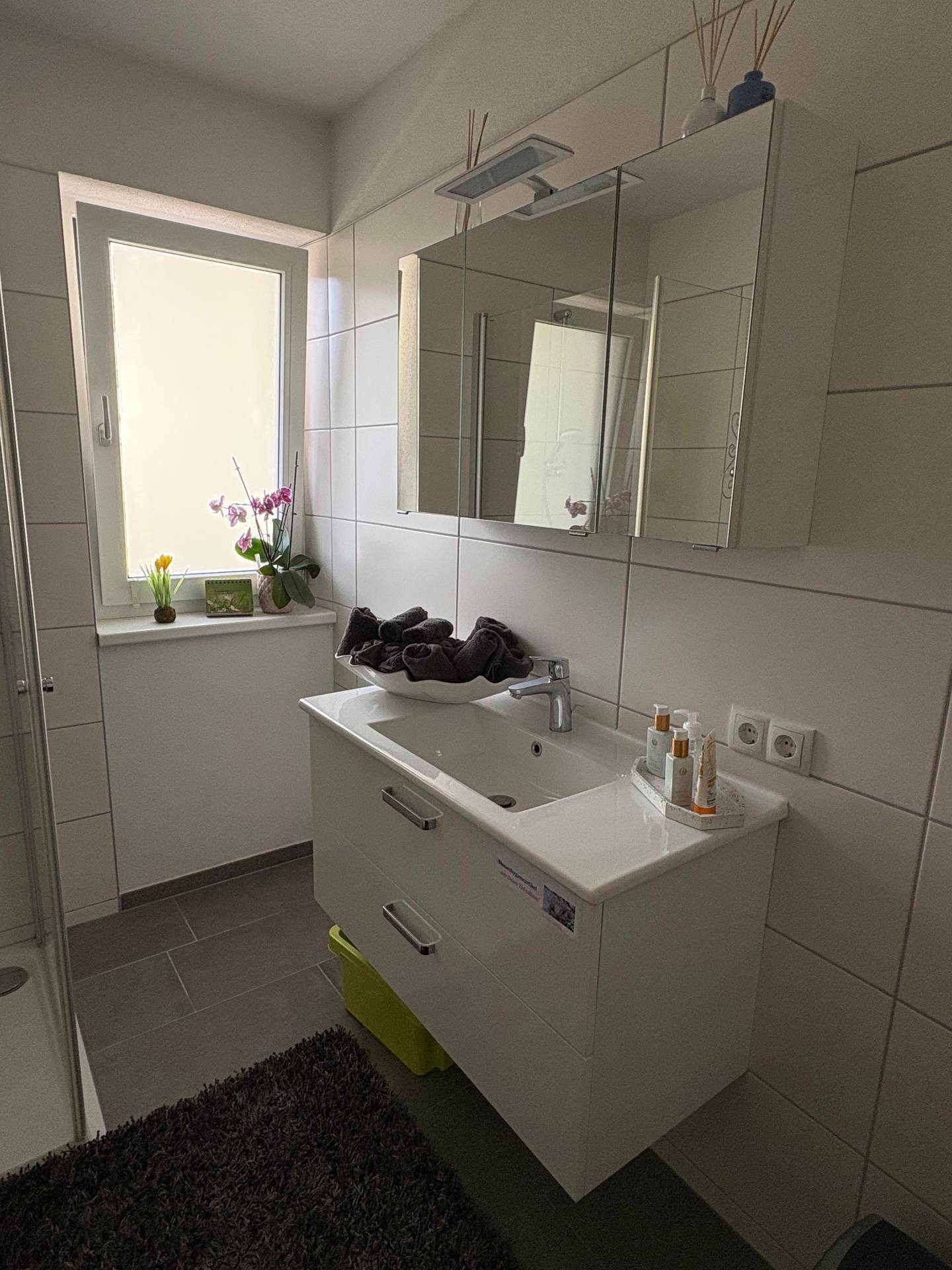 Modernes Badezimmer mit Waschtischunterschrank, Spiegelschrank und einem Fenster für natürliches Licht.