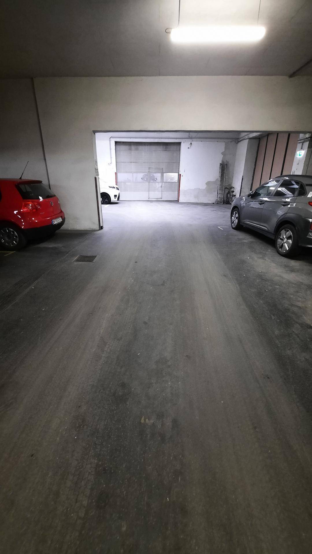 Tiefgarage mit Betonboden und geparkten Autos, die zu einem Rolltor führt.