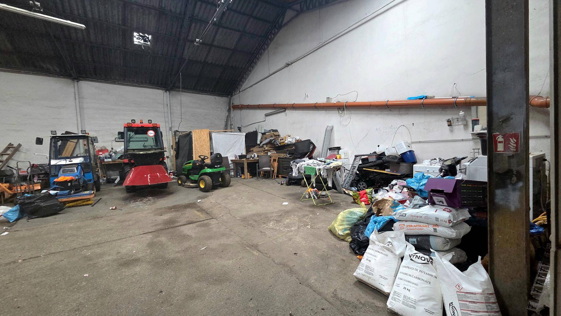 Weitläufige Lagerhalle mit hohen Decken, Oberlichtern und verschiedenen Geräten und Unordnung auf dem Boden.