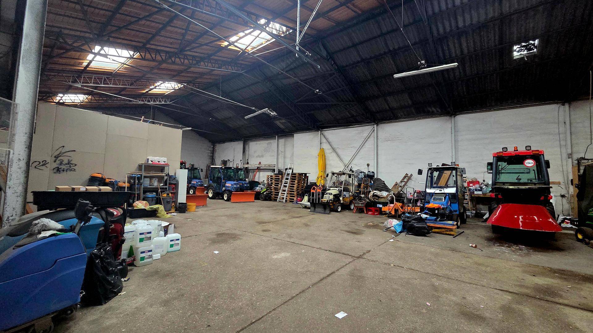 Große Lagerhalle mit hohen Decken, Oberlichtern und verschiedenen Geräten und Materialien auf dem Betonboden.