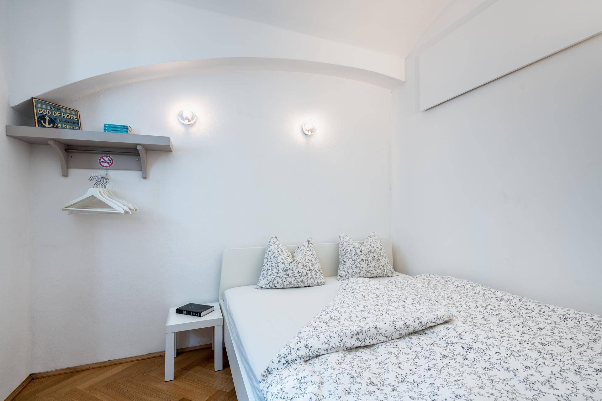 Helles Schlafzimmer mit Doppelbett, Nachttisch und Wandregal in minimalistischem Stil.