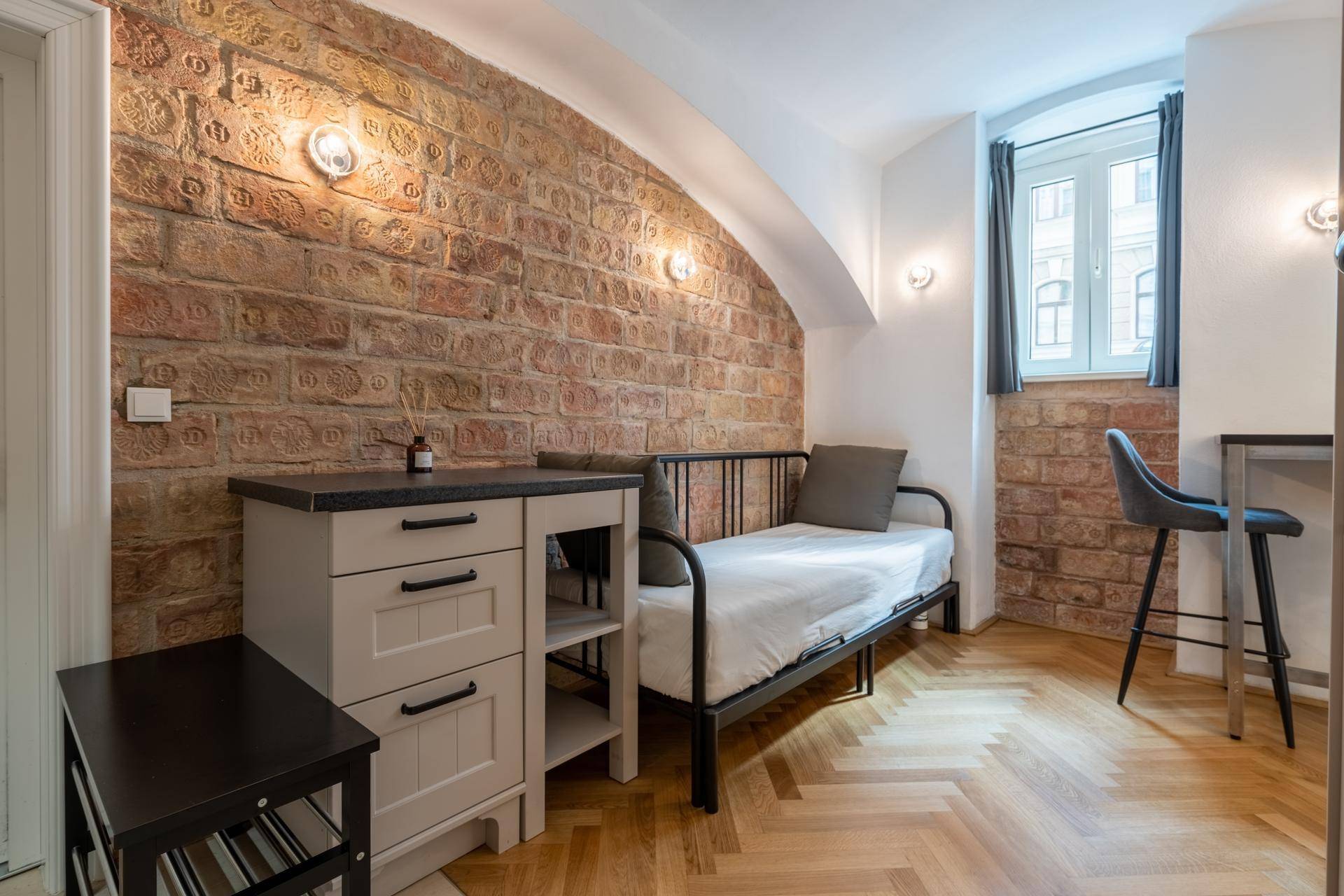 Gemütliches Schlafzimmer mit Einzelbett, Kommode und charakteristischer Ziegelwand.