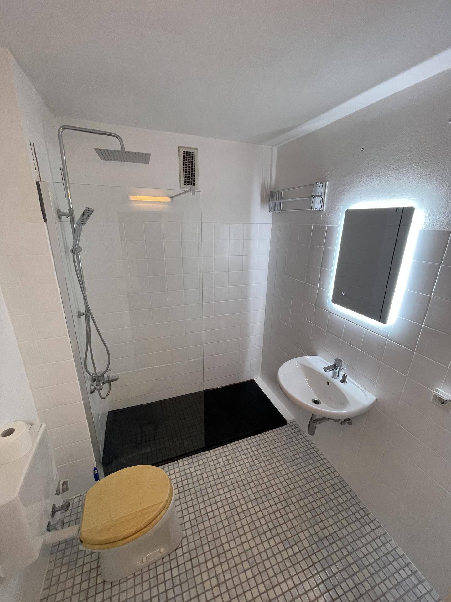 Modernes Badezimmer mit weiß gefliesten Wänden, ebenerdiger Dusche und beleuchtetem Spiegel.