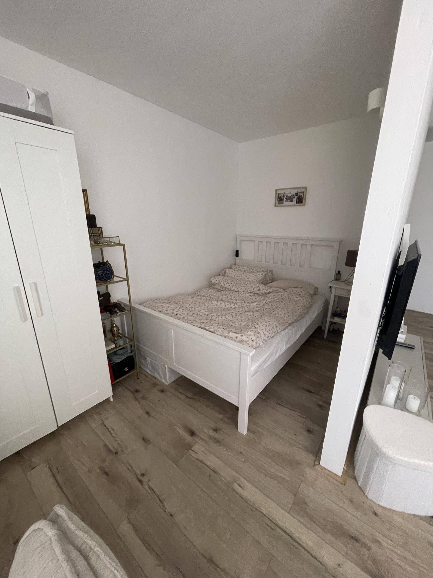 Helles Schlafzimmer mit weißem Bett, Kleiderschrank und Fernseher.
