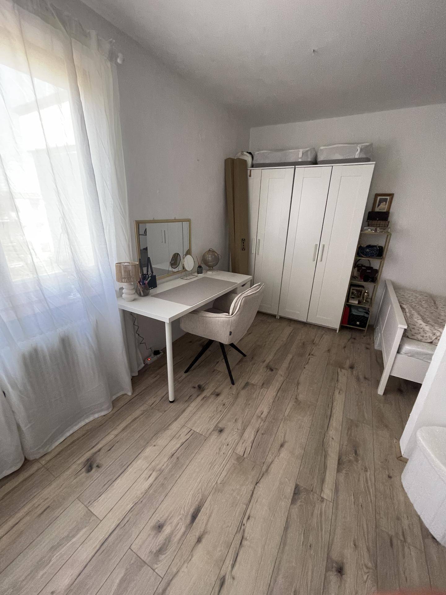 Schlafzimmer mit Schreibtisch, weißem Kleiderschrank und hellem Holzboden.