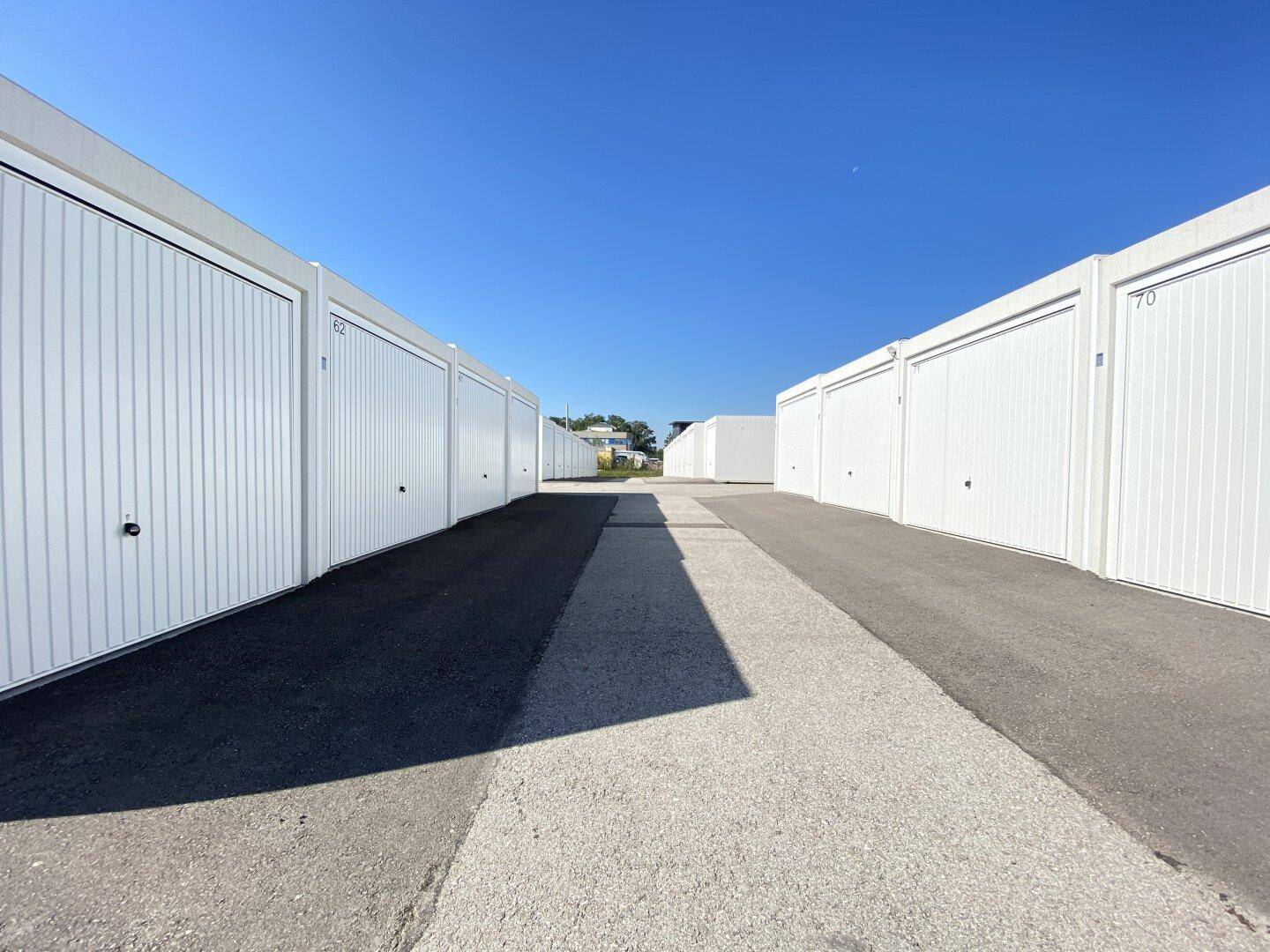 Weitere Ansicht der modernen weißen Garagenreihen unter klarem Himmel mit asphaltiertem Zufahrtsweg.