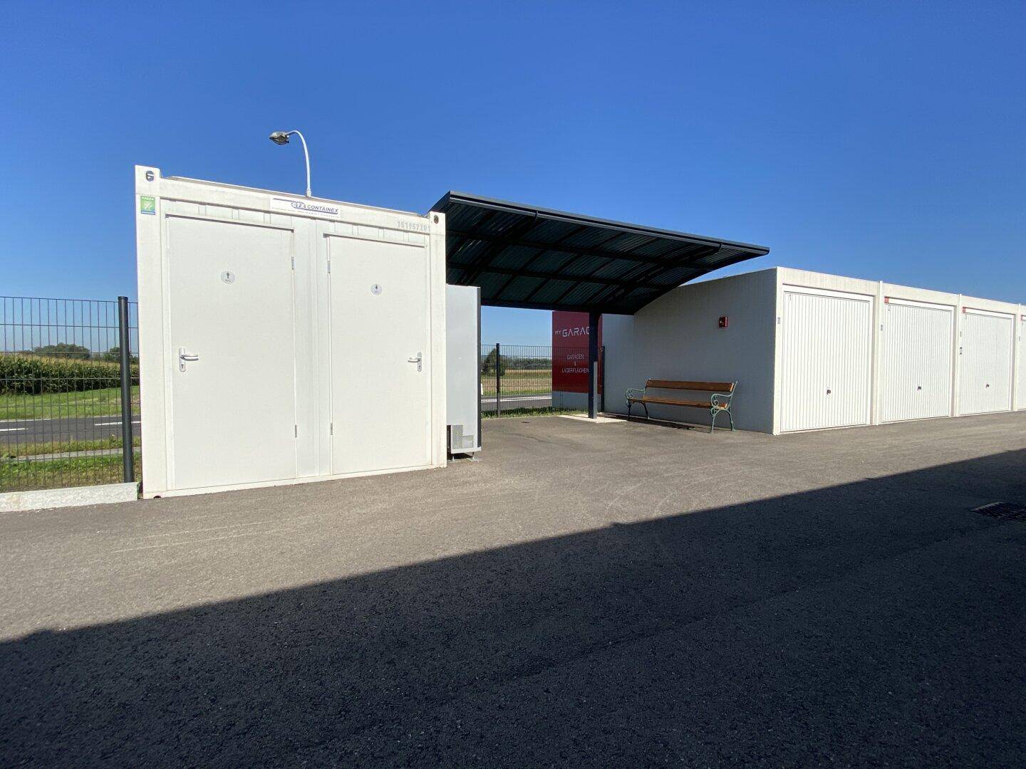 Eingangsbereich der Lagerhallen mit überdachtem Wartebereich, Sitzbank und weiteren Garageneinheiten.