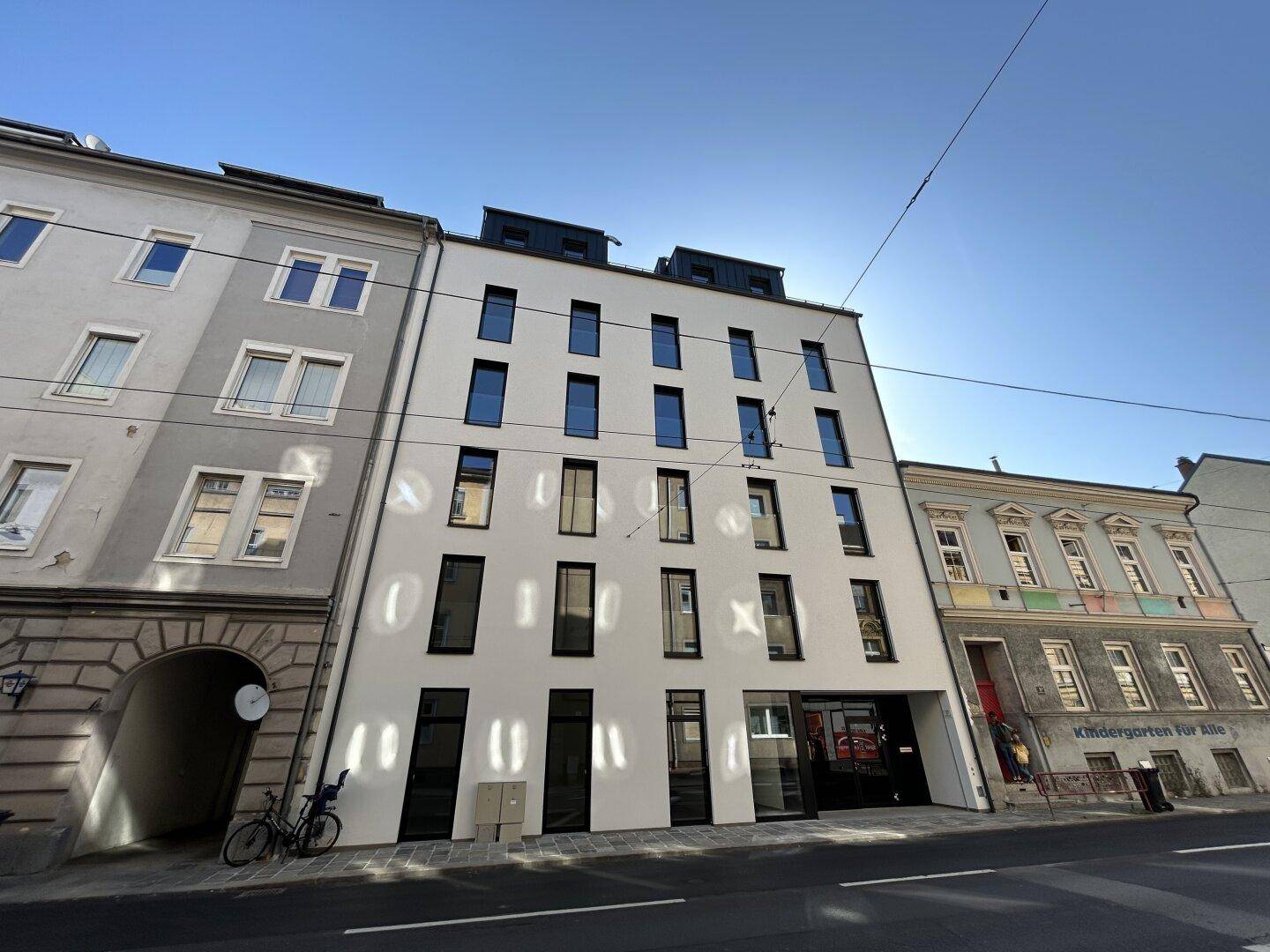 Moderne Fassade eines Neubaus an einer städtischen Straße mit klarem Himmel.