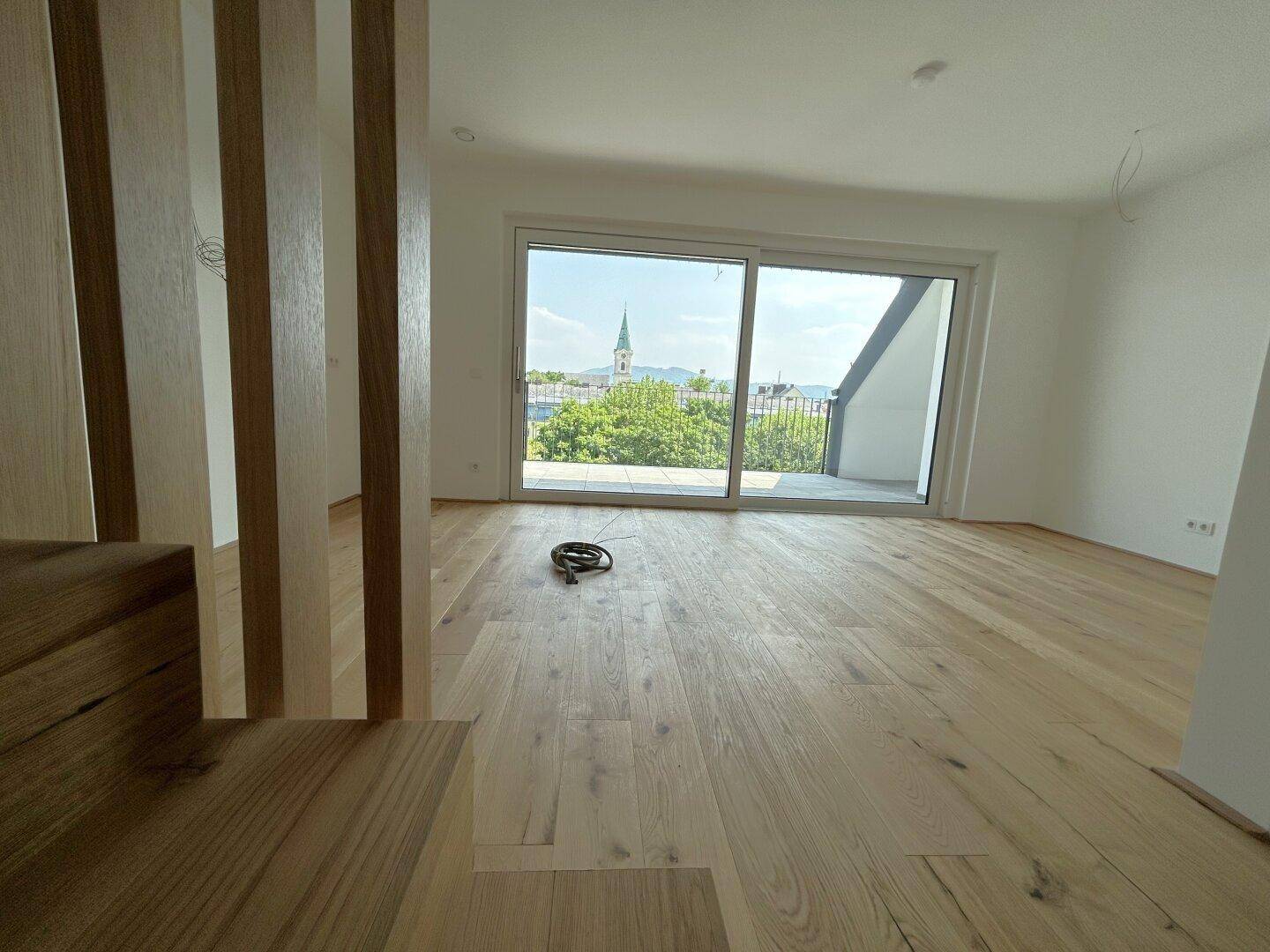 Heller Wohnbereich mit Eichenparkettboden und großem Schiebefenster mit Stadtblick.