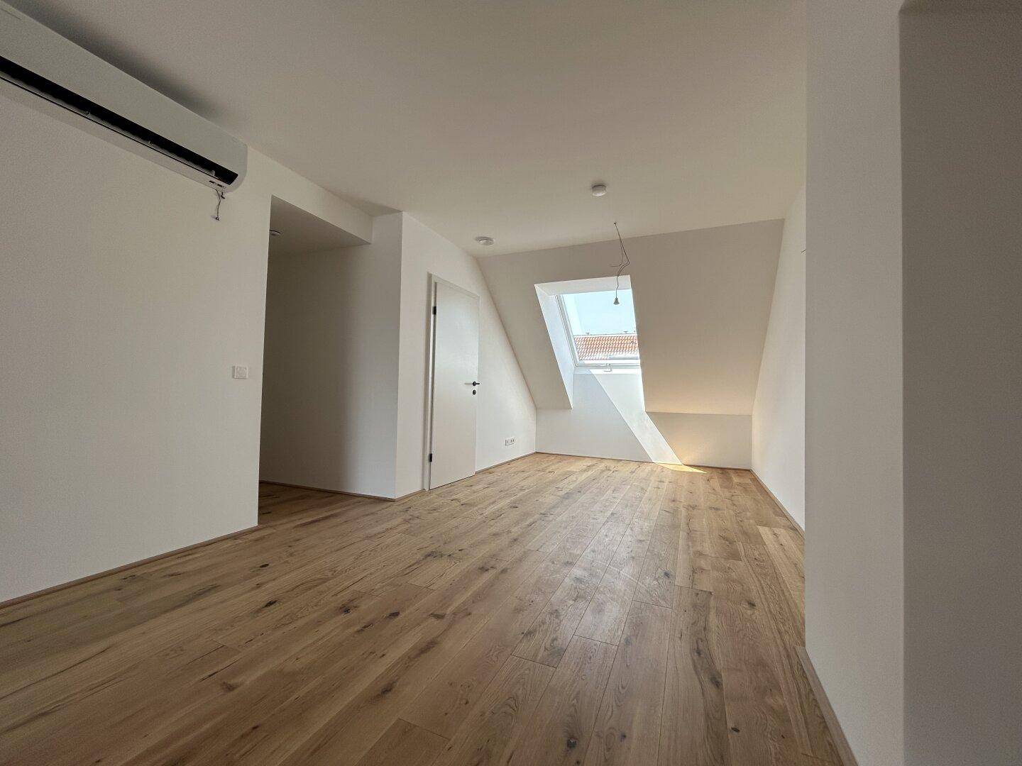 Helles Dachzimmer mit Holzboden, Dachschräge und einem großen Dachfenster.