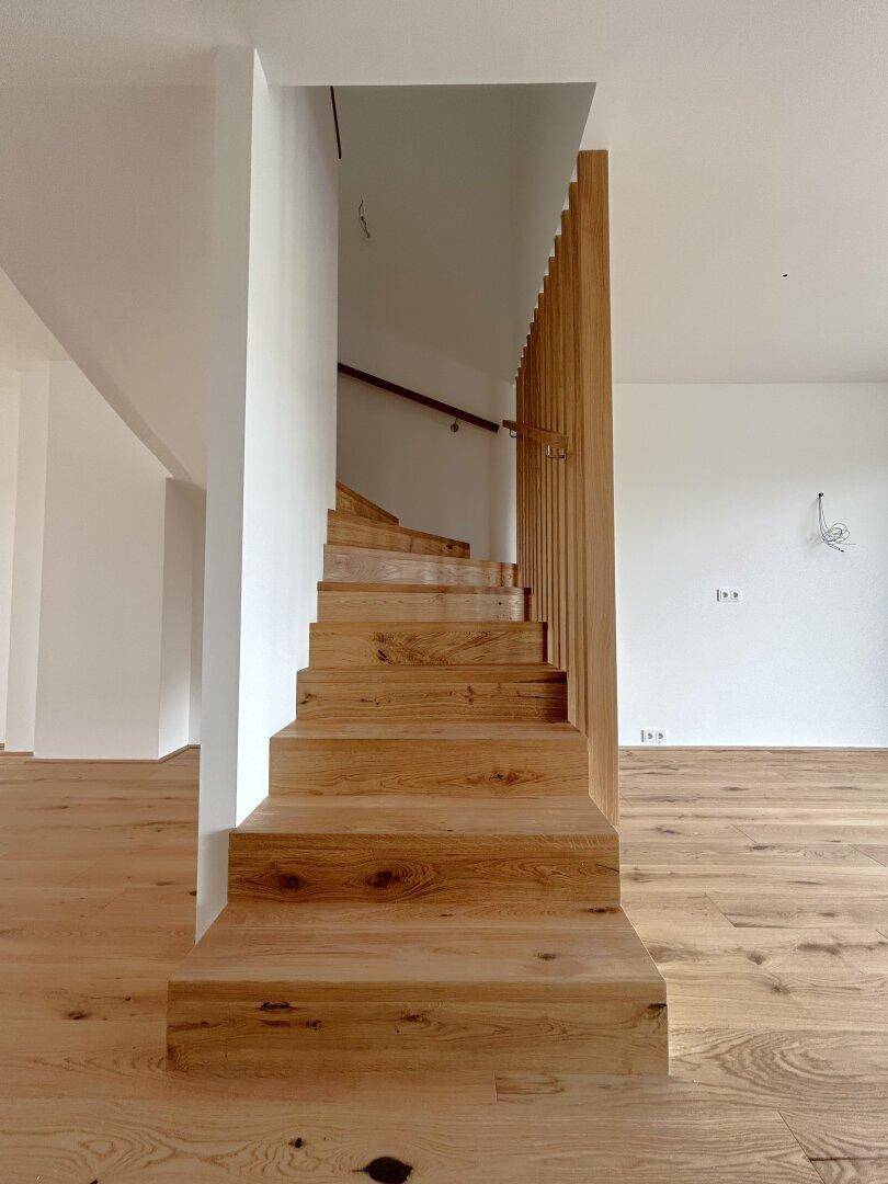 Elegante Holztreppe mit passendem Eichenparkettboden in einem hellen Eingangsbereich.