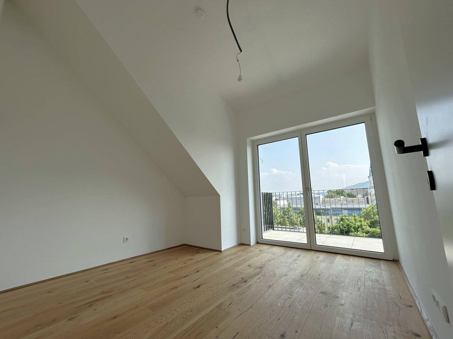 Helles Schlafzimmer mit Eichenparkett, Dachschräge und Balkontür mit Stadtblick.
