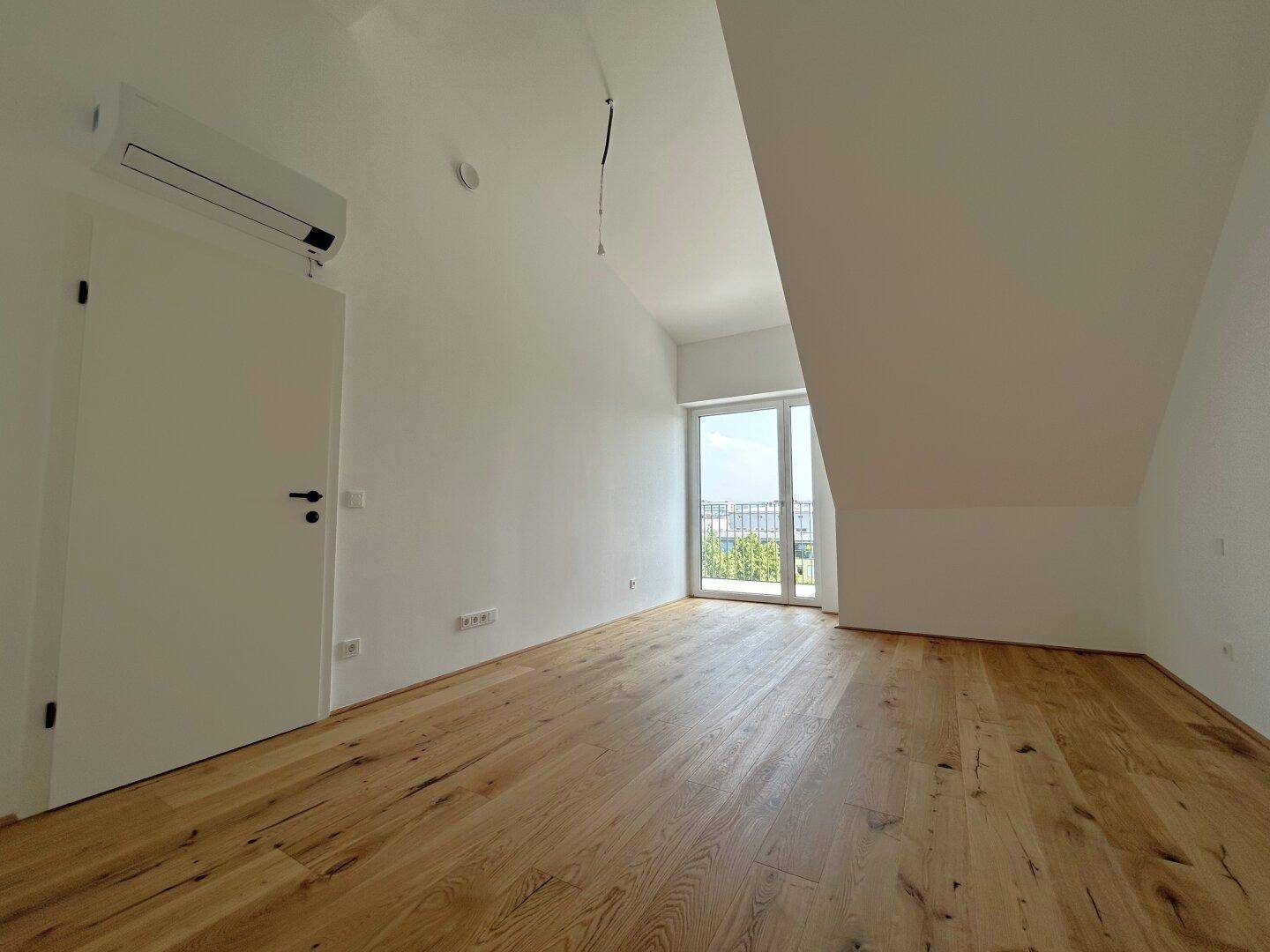 Geräumiges Schlafzimmer mit Eichenparkett, Dachschräge und Zugang zum Balkon.