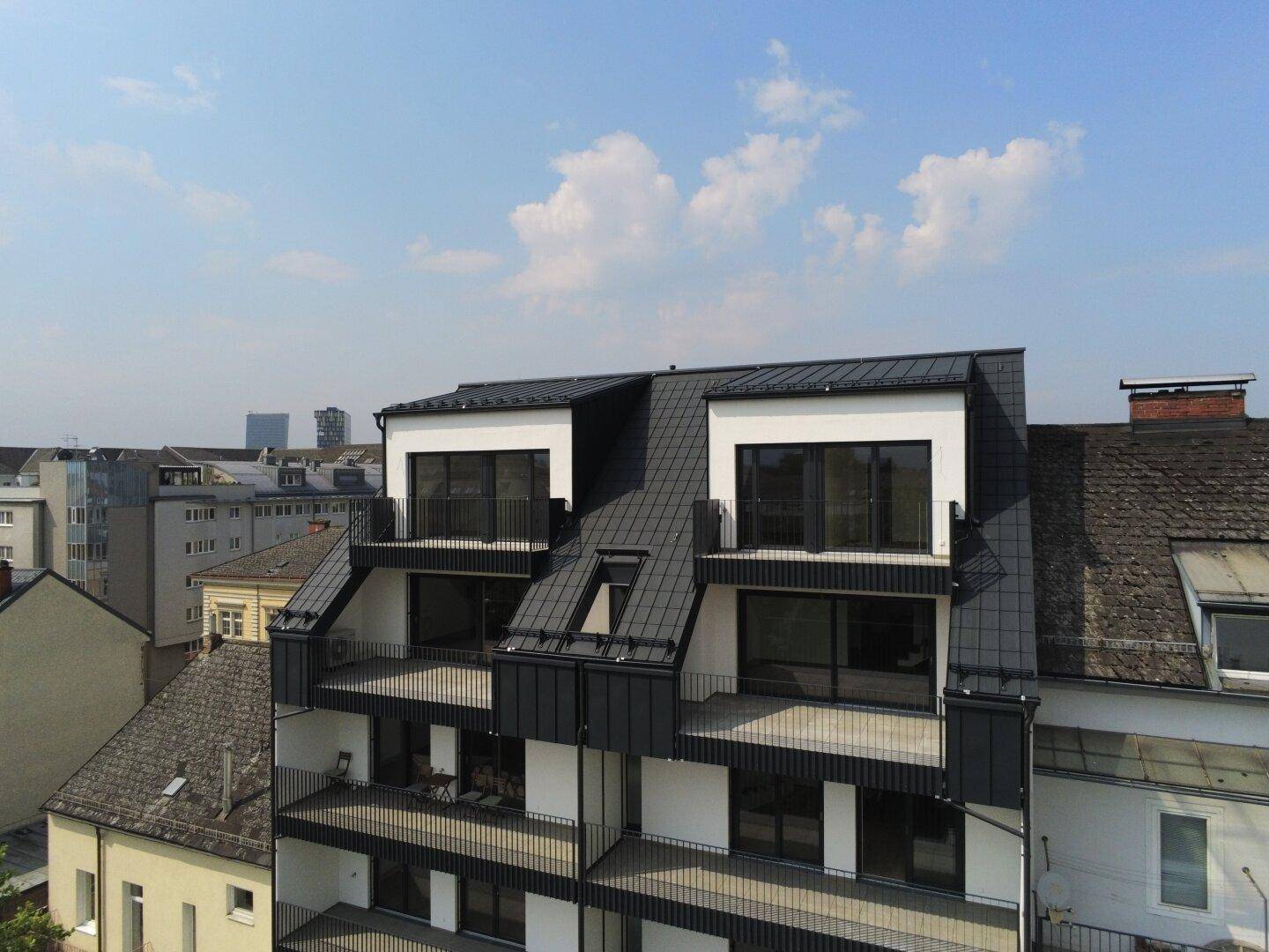 Moderne Architektur eines Neubaus mit Mansarddach und Balkonen in städtischer Umgebung.