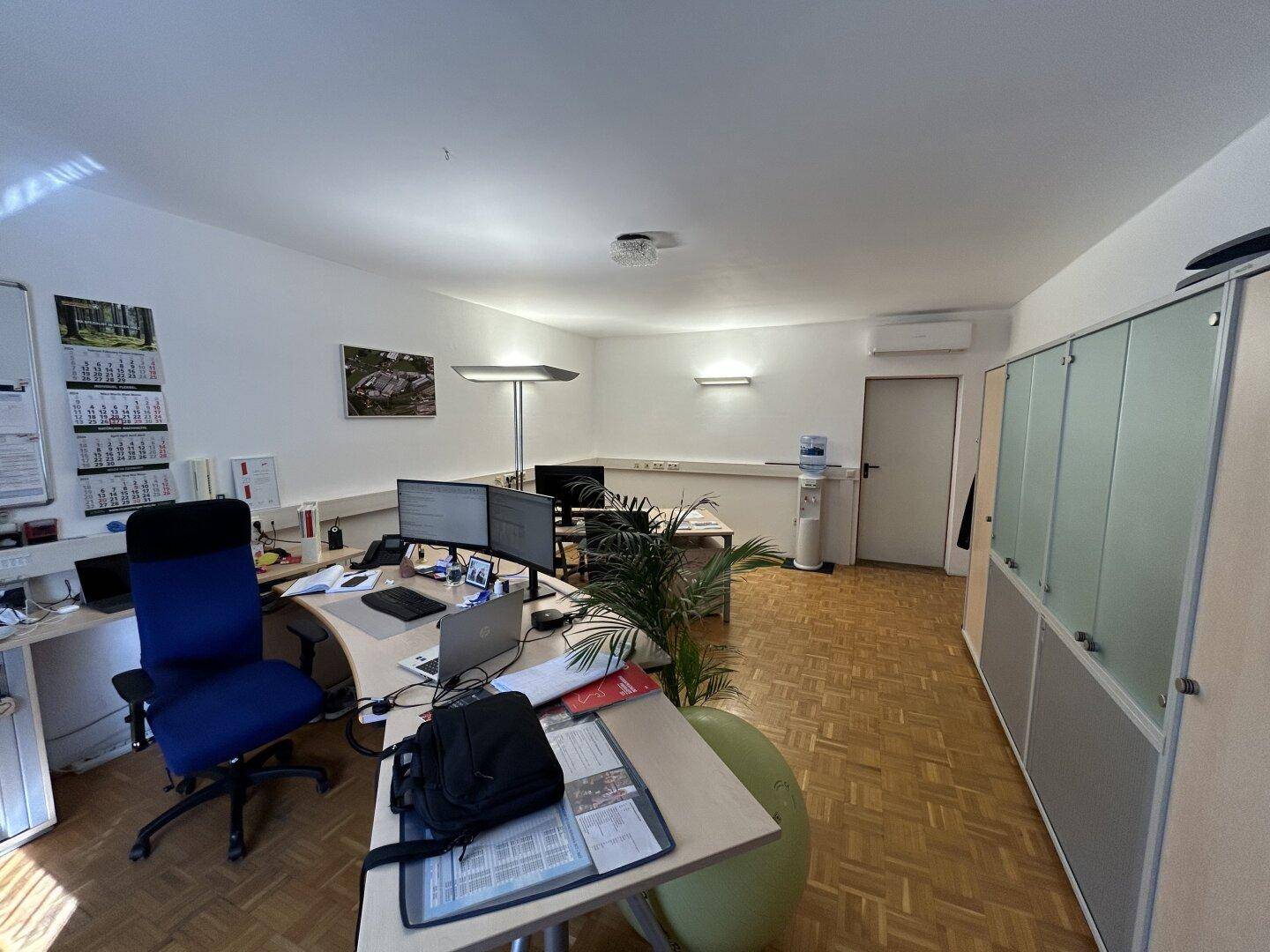 Helles und geräumiges Büro mit mehreren Arbeitsplätzen, Holzparkettboden und modernen Büromöbeln.