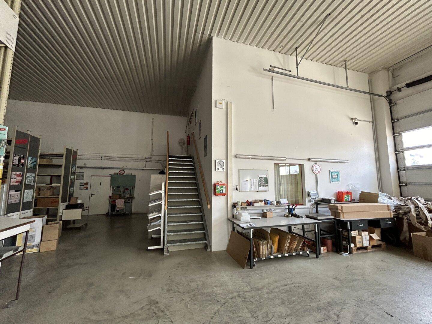 Bereich innerhalb der Lagerhalle mit einer Treppe zum Obergeschoss und einem Arbeitsplatz mit Schreibtisch.