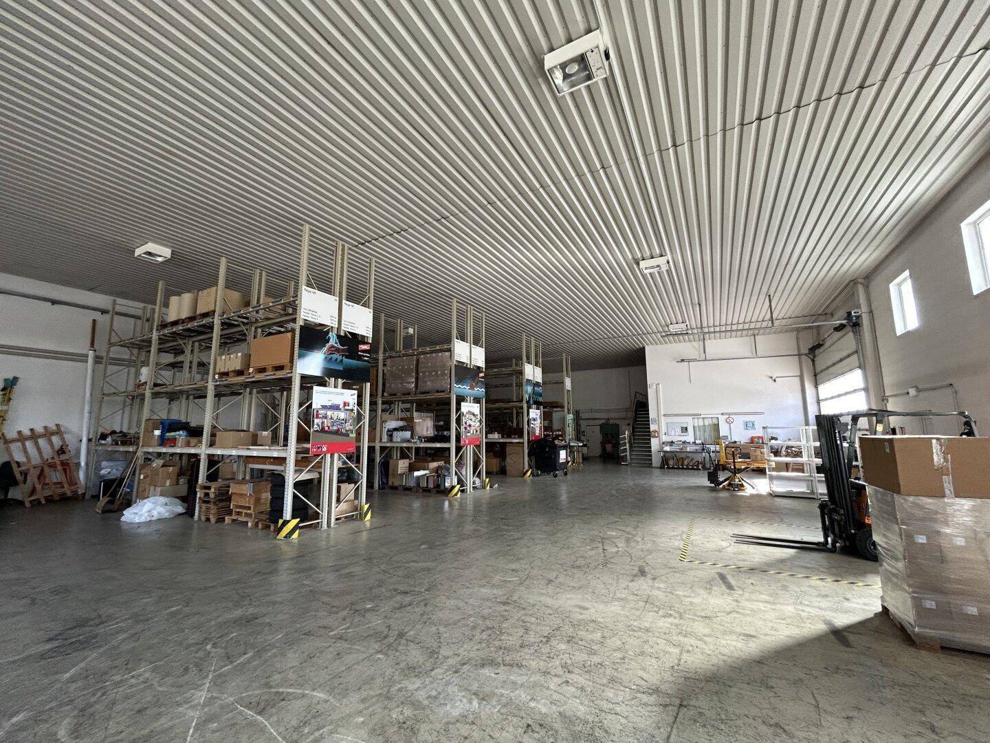 Innenansicht der Lagerhalle mit hohen Regalen voller Kartons und einem Gabelstapler auf dem Betonboden.