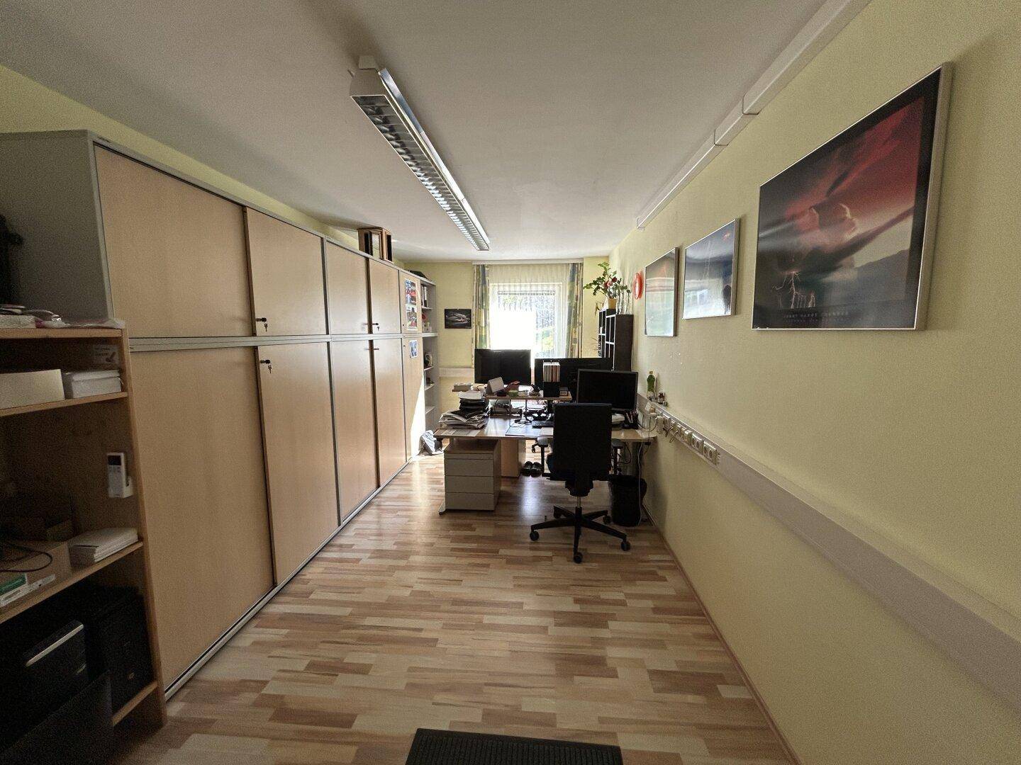 Langes Büro mit durchgehenden Schränken entlang einer Wand und mehreren Arbeitsplätzen mit Blick nach draußen.