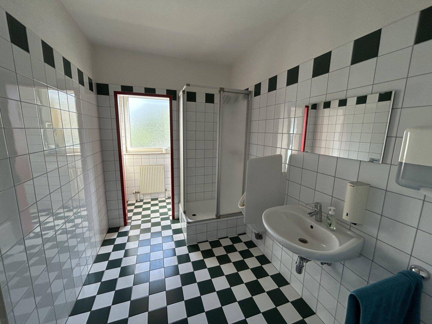 Badezimmer mit markantem schwarz-weiß kariertem Fliesenboden, einer Duschkabine und einem Fenster.