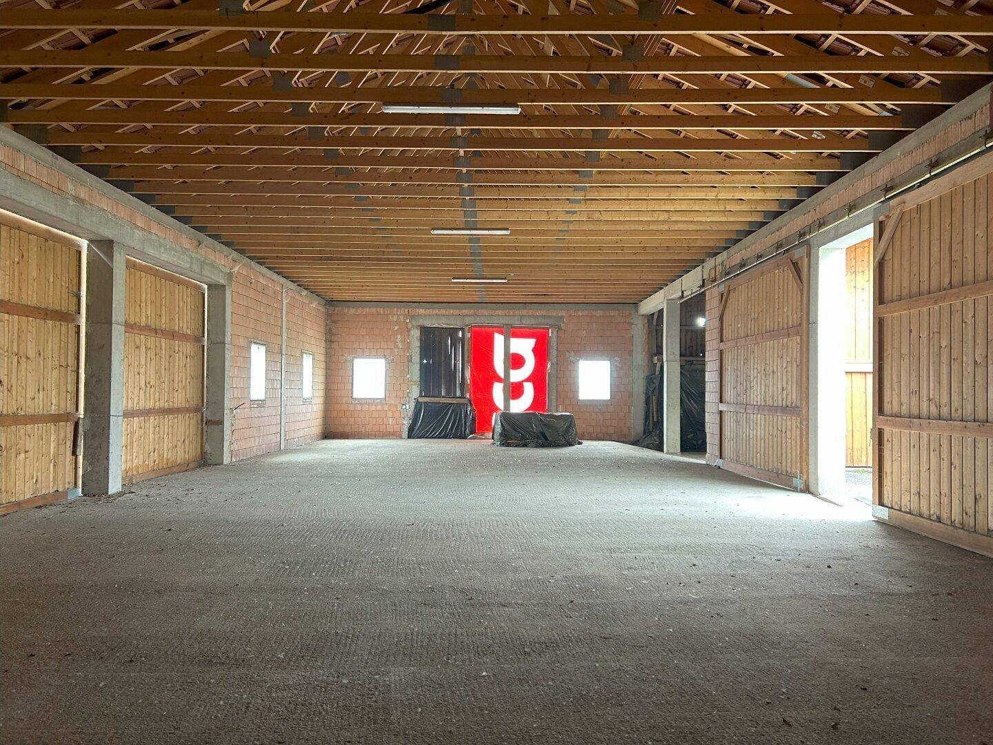 Geräumiger Innenbereich mit Holzdachkonstruktion, Ziegelwänden und großen Holztoren, bereit für Ausbau.