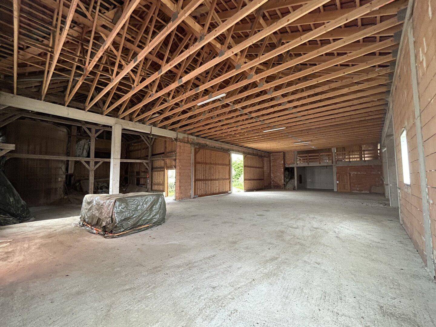 Großer, leerer Innenraum mit sichtbaren Holzbalken und Ziegelwänden, ideal für Lager oder Werkstatt.