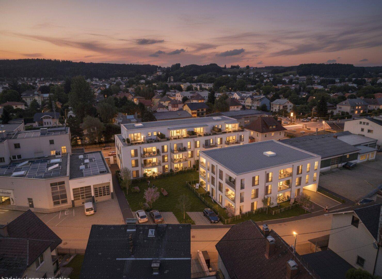 Abendliche Luftaufnahme eines modernen Wohnkomplexes mit beleuchteten Balkonen und umliegender Bebauung.