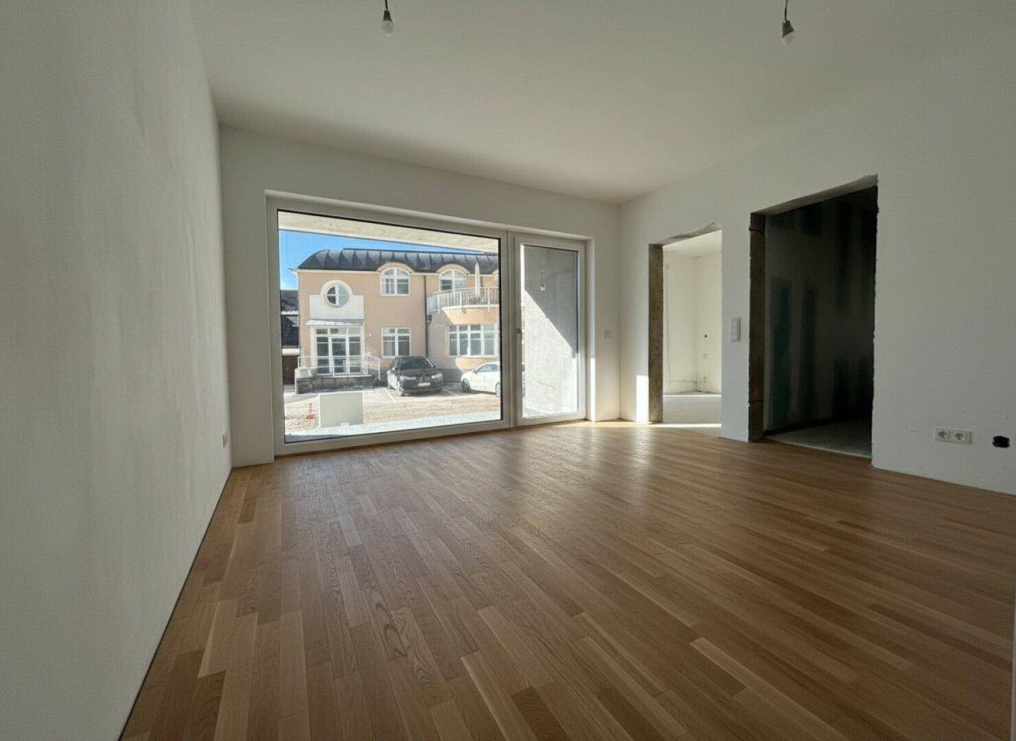 Heller Wohnraum mit neuem Parkettboden und großen Fenstern, die viel Tageslicht hereinlassen.