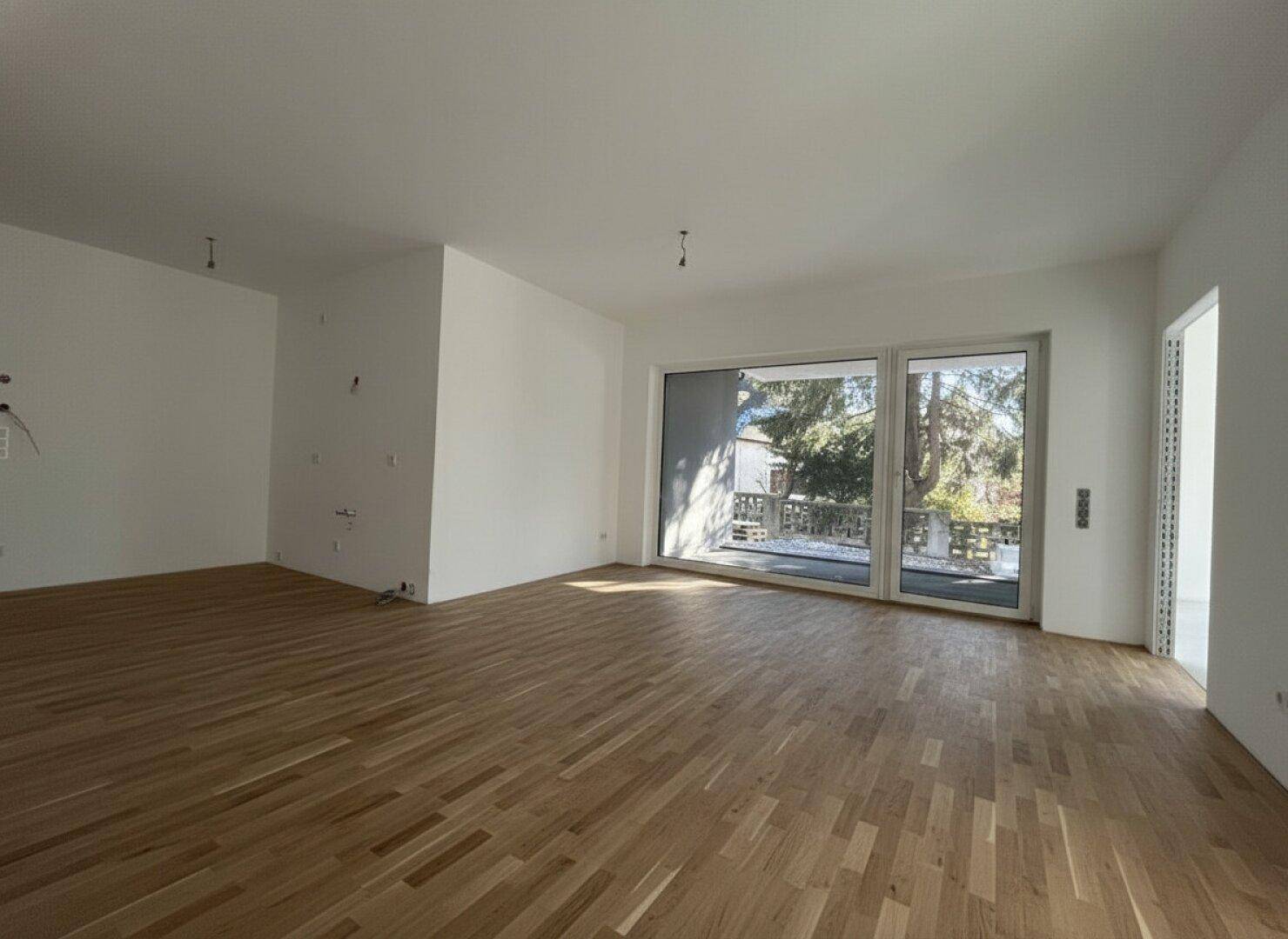 Heller, geräumiger Wohnbereich mit neuem Parkettboden und großen Glas-Schiebetüren, die viel Tageslicht hereinlassen.