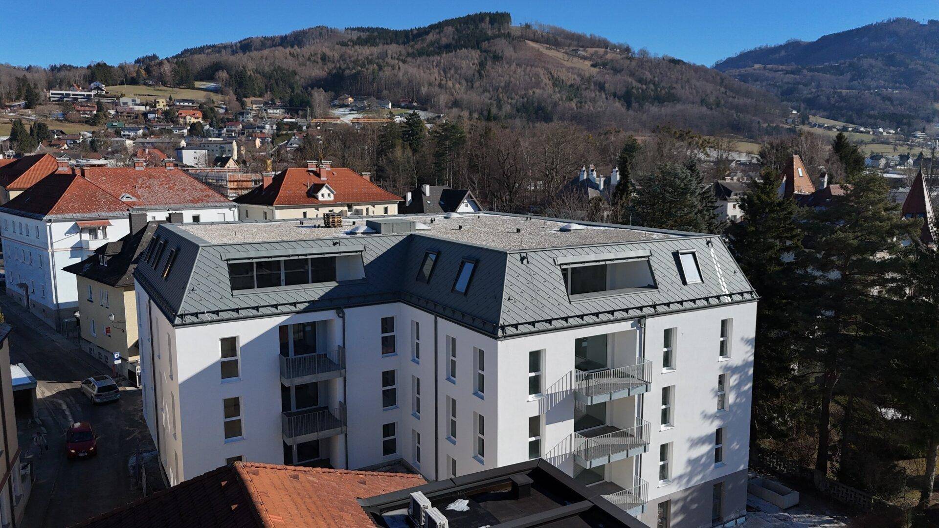 Neubau-Wohngebäude mit Mansarddach und Balkonen, eingebettet in eine städtische Landschaft.
