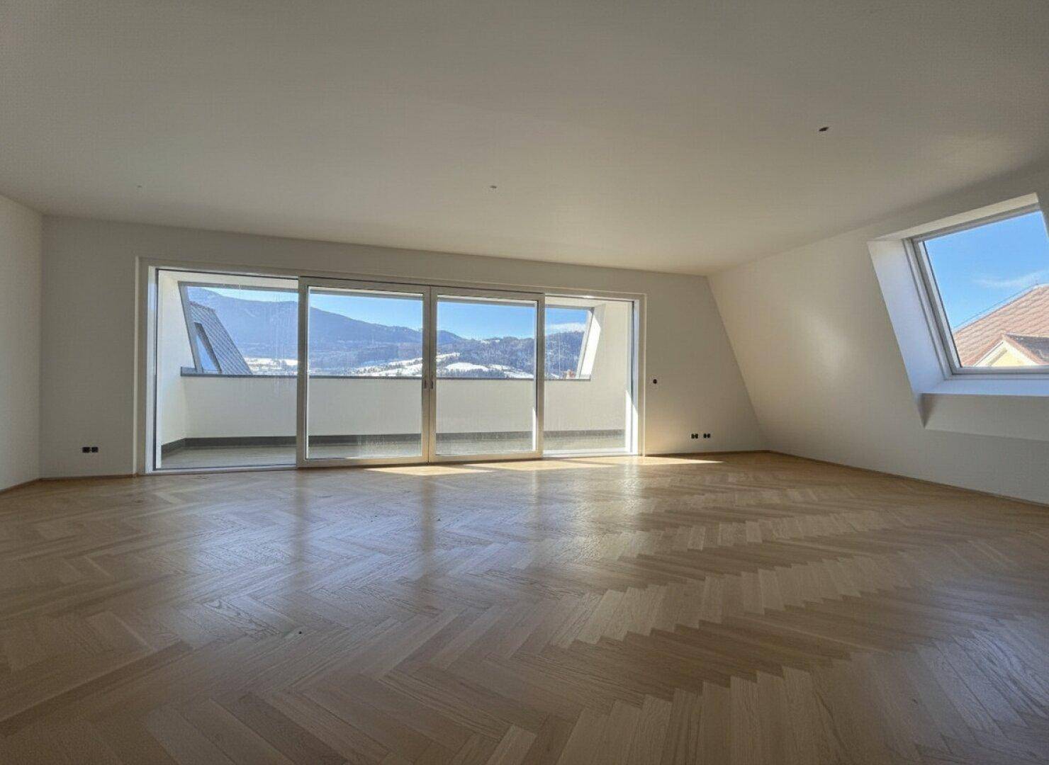 Geräumiges Zimmer mit hellem Fischgrätparkett und Zugang zu einem Balkon mit Bergsicht.