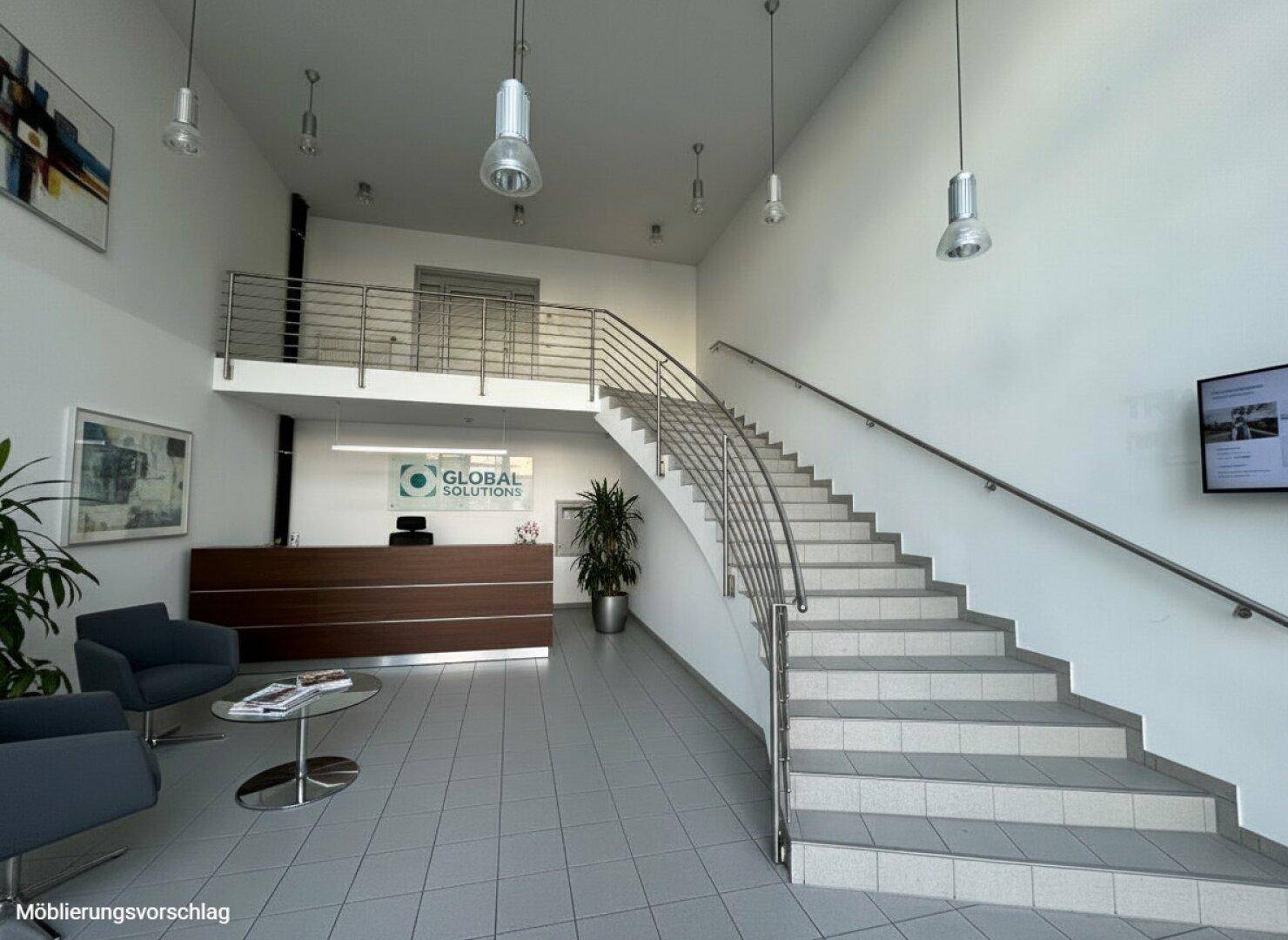 Geräumige Lobby mit Empfangsbereich, moderner Treppe und Sitzgelegenheiten für Besucher.