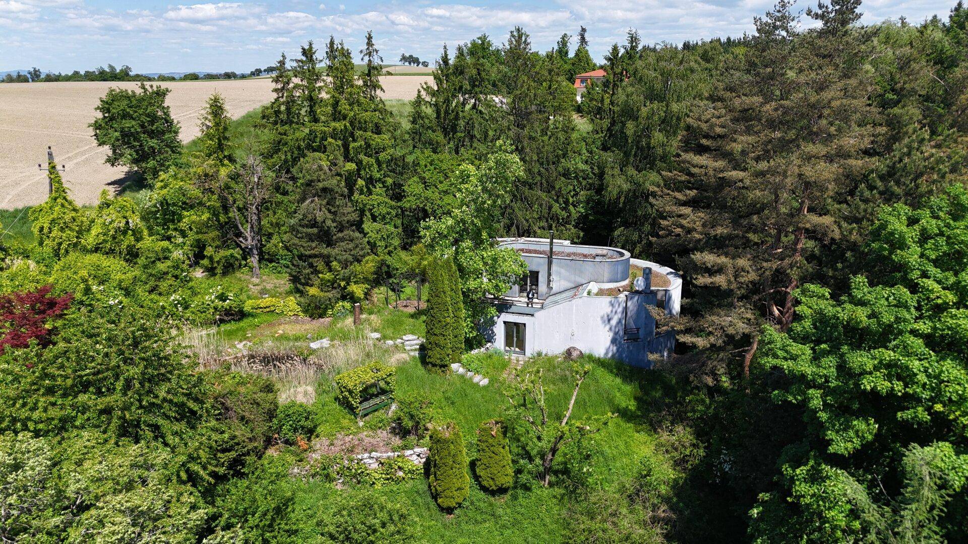 Panoramablick auf ein modernes Wohnhaus, eingebettet in eine grüne Hügellandschaft mit angrenzenden Feldern.