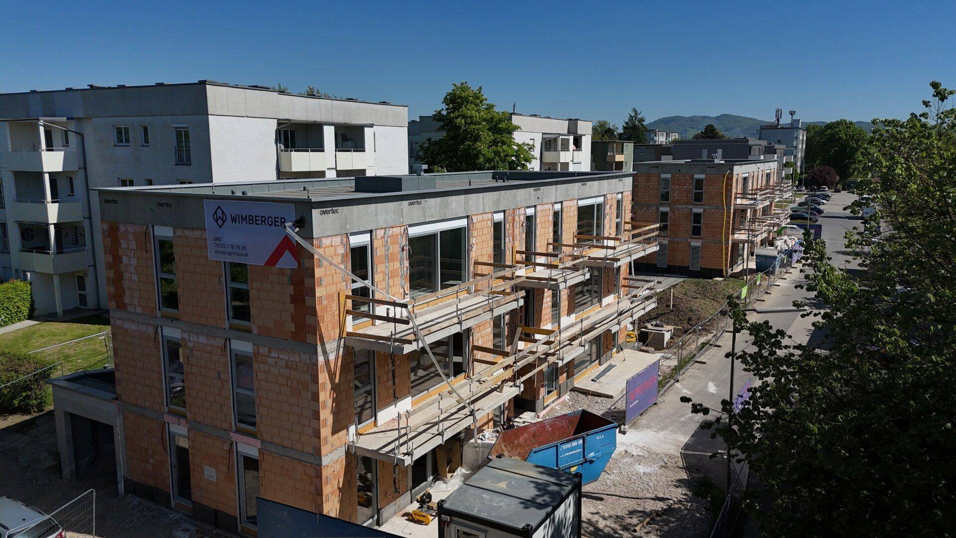 Neubauwohnungen im Rohbau mit Gerüsten und Blick auf die umliegende Wohnsiedlung.