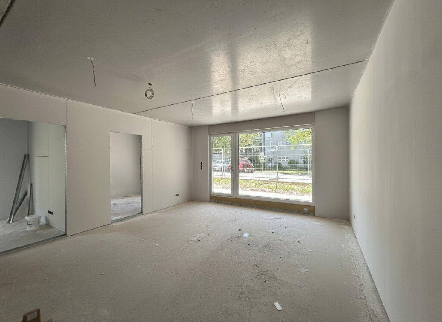 Unfertiger Wohnraum im Neubau mit großen Fenstern und Blick ins Grüne.
