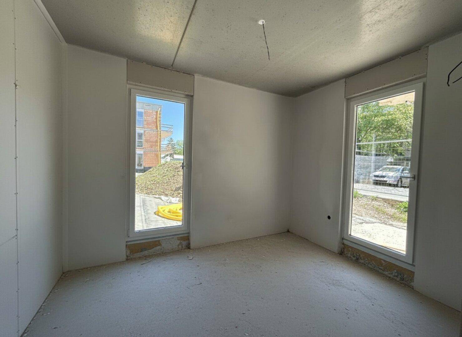 Unfertiges Zimmer mit zwei hohen Fenstern und Blick auf die Baustelle.