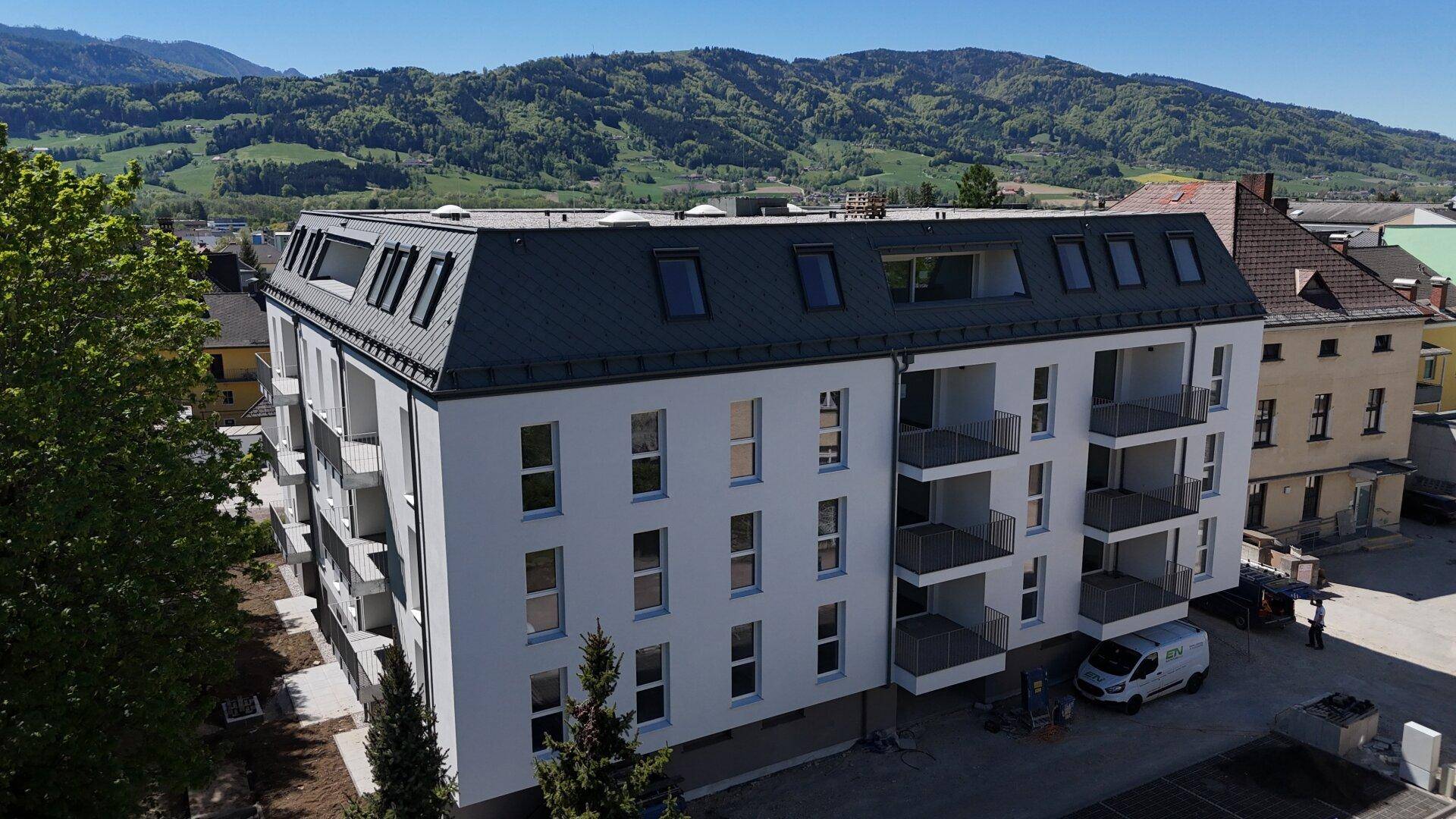 Ansicht des modernen Mehrfamilienhauses mit Balkonen und Dachfenstern in sonniger Umgebung.