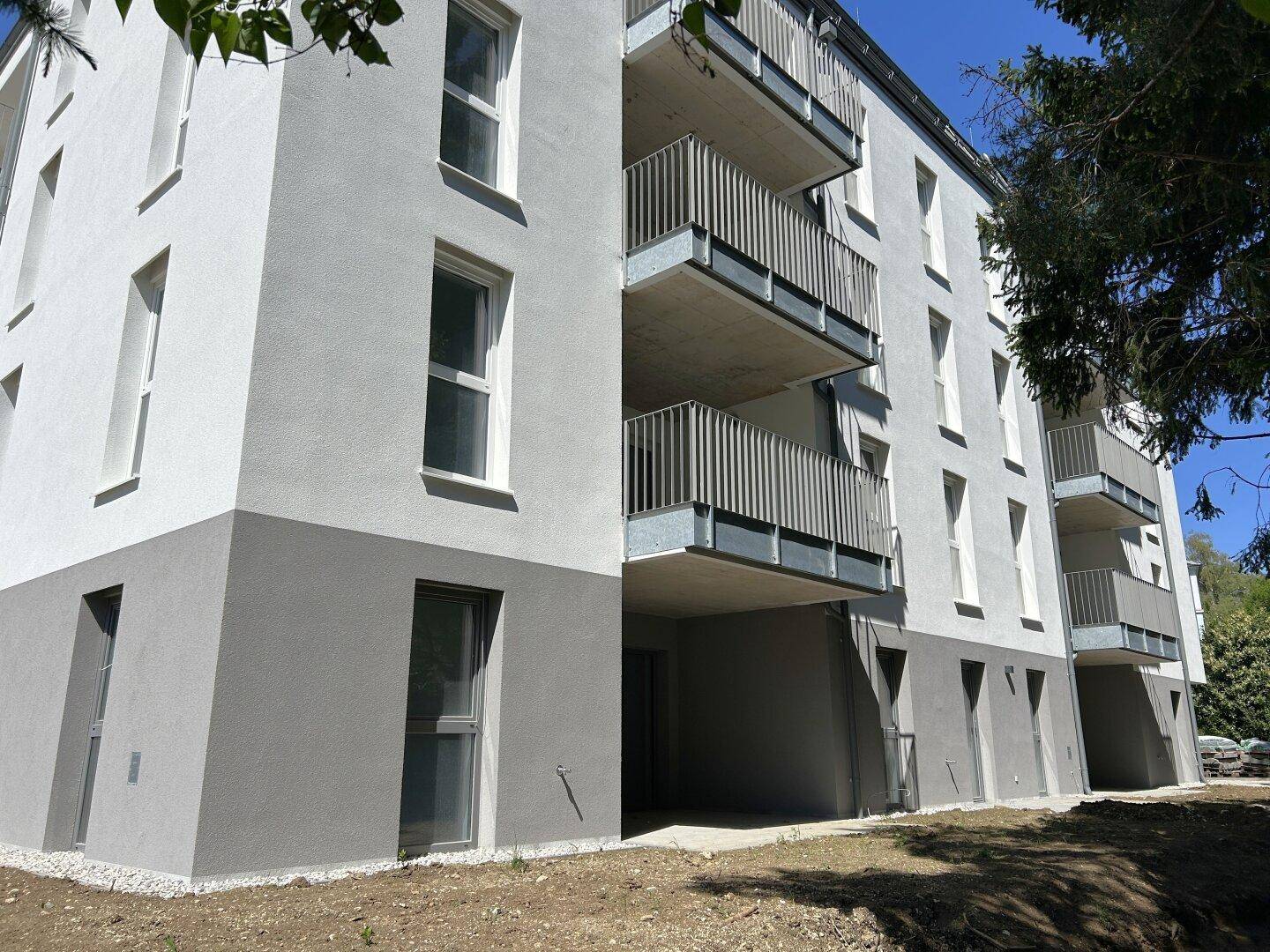 Moderne Gebäudefassade mit weißem und grauem Putz sowie Balkonen in einem Neubau.