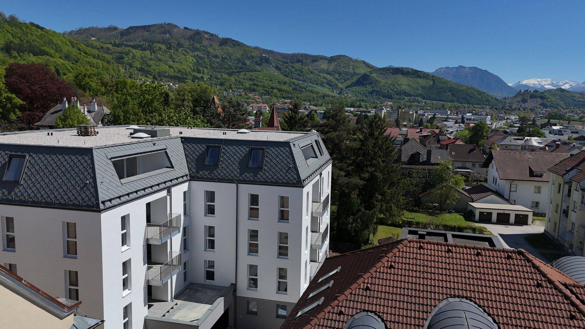 Luftaufnahme eines modernen Wohngebäudes mit Balkonen und Blick auf die umliegende Berglandschaft.